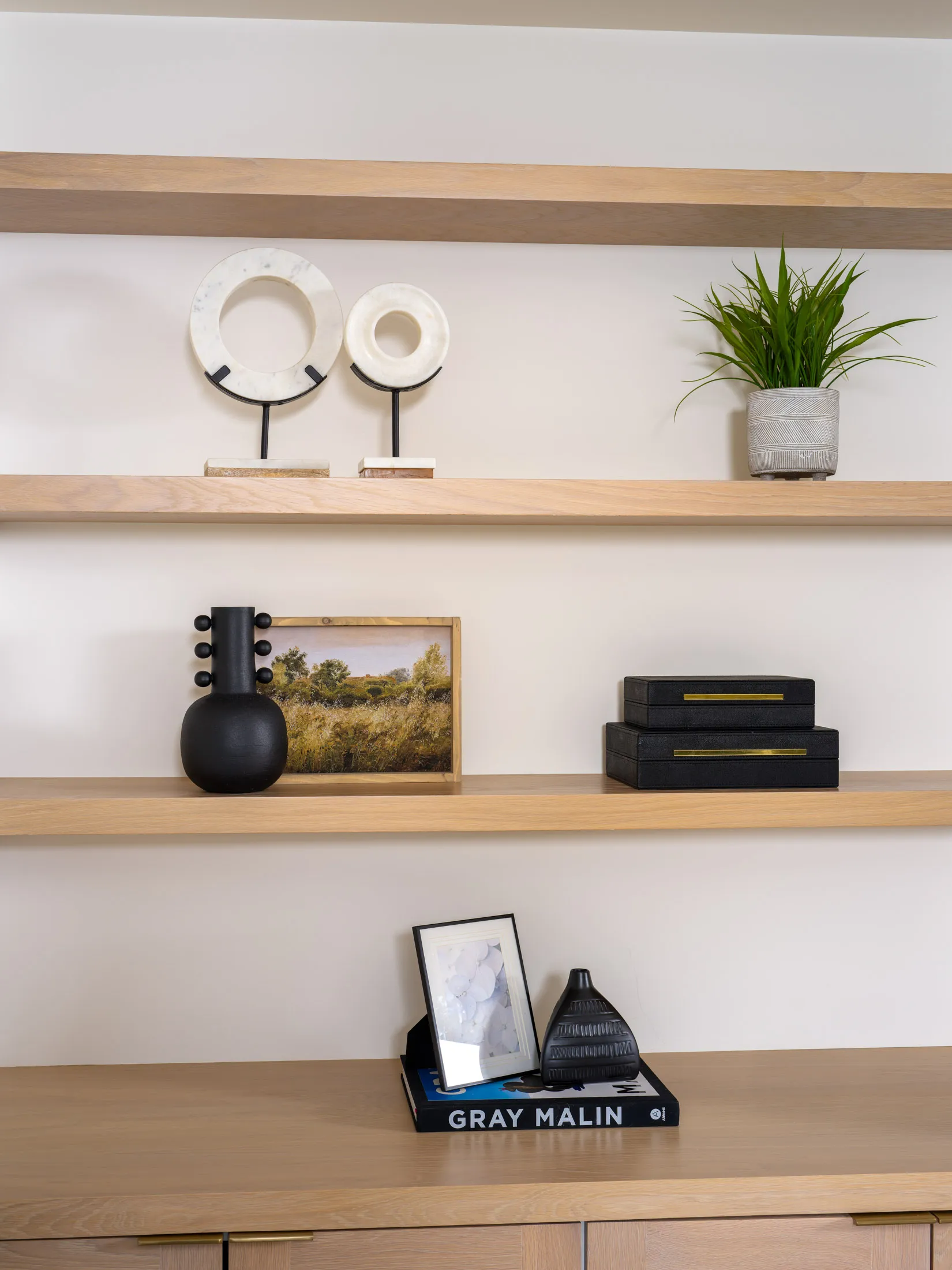 Light wood shelves with circular marble sculptures, a small plant, and black decorative pieces in a minimal arrangement.