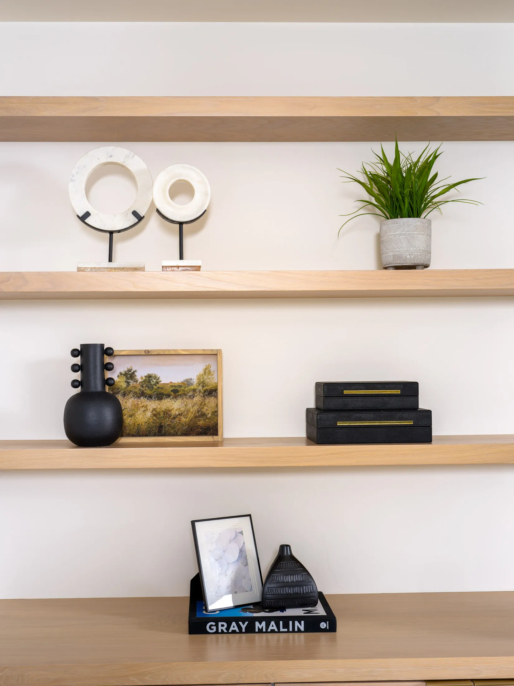 Light wood shelves showcasing circular marble sculptures, a small potted plant, and black decorative pieces against a white backdrop.