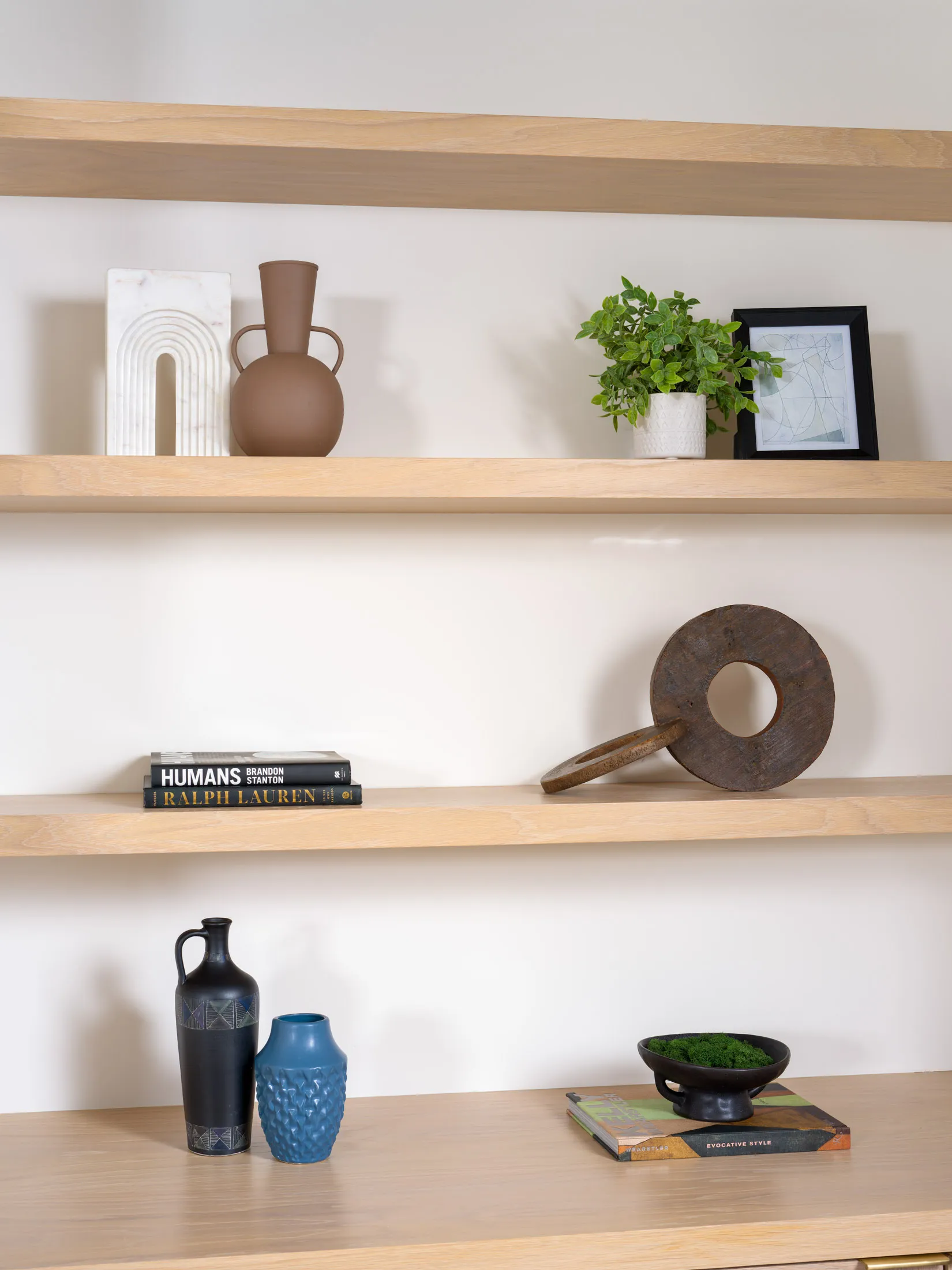 Wooden built-in shelves displaying various decorative objects, including vases, a marble arch sculpture, and a small plant.
