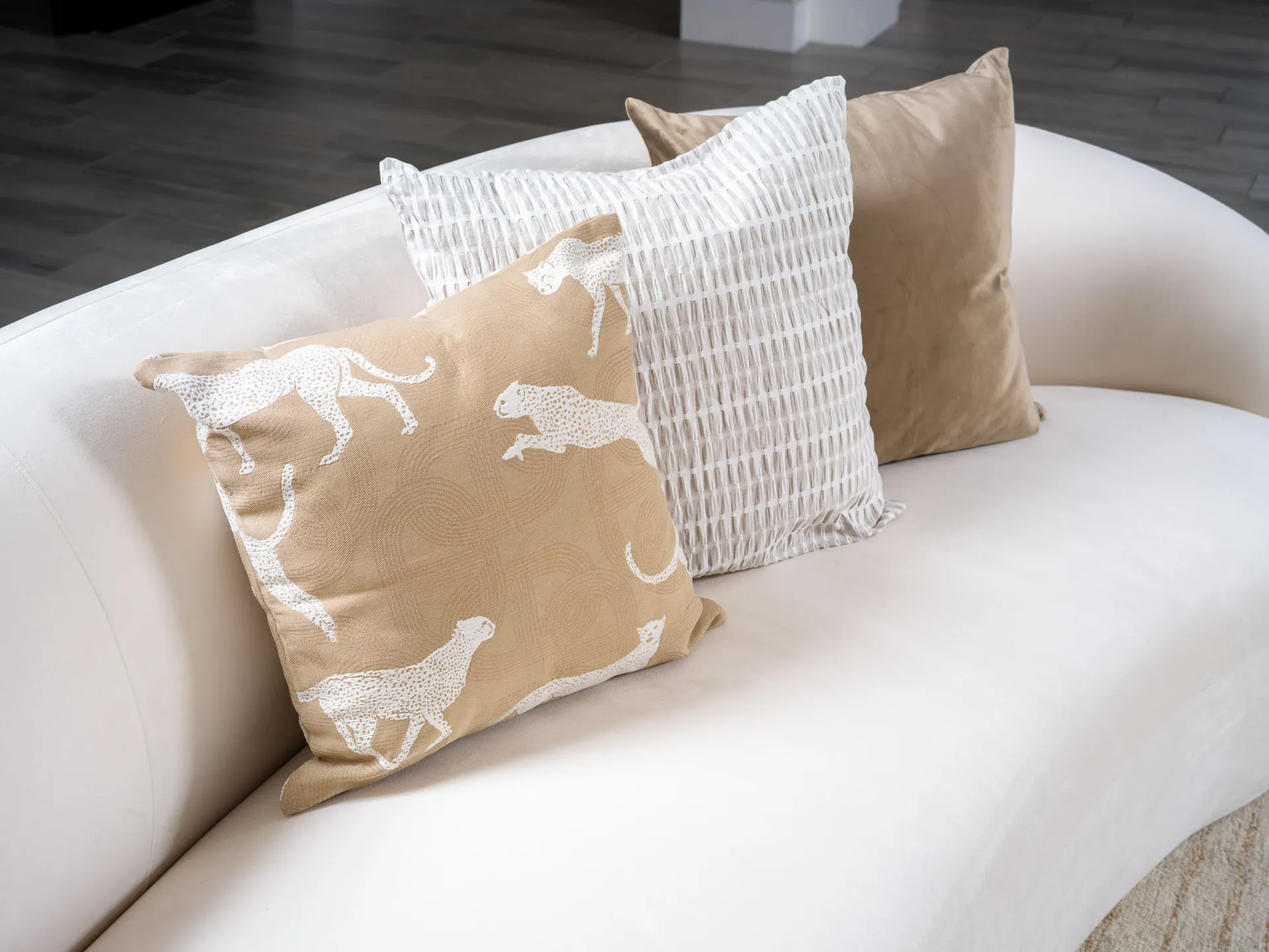 A trio of neutral pillows placed on a curved white sofa. One features a playful white cheetah pattern on tan fabric.