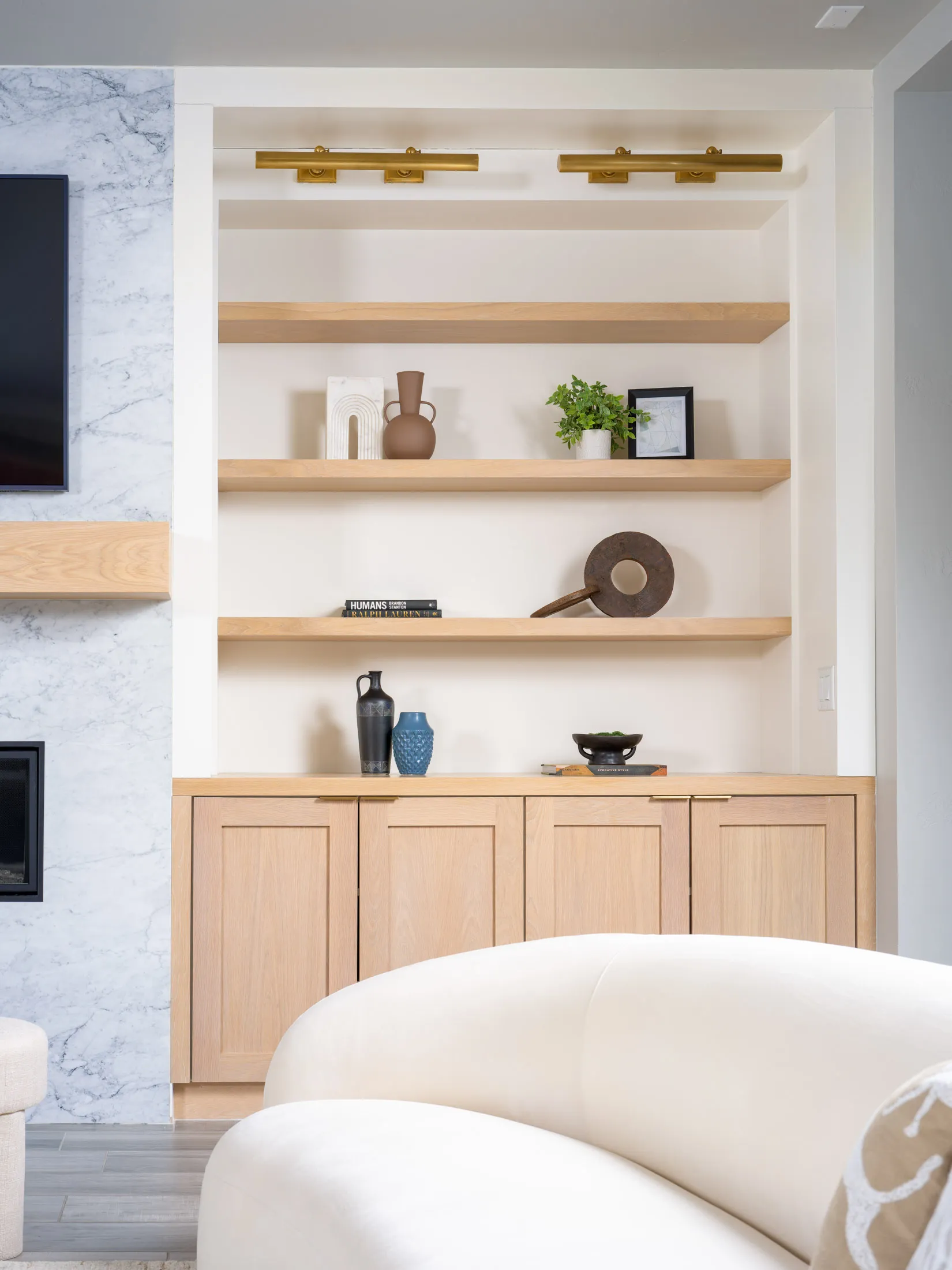 Built-in shelves with curated decor pieces, soft lighting, and natural wood cabinets in a luxury staged living room.