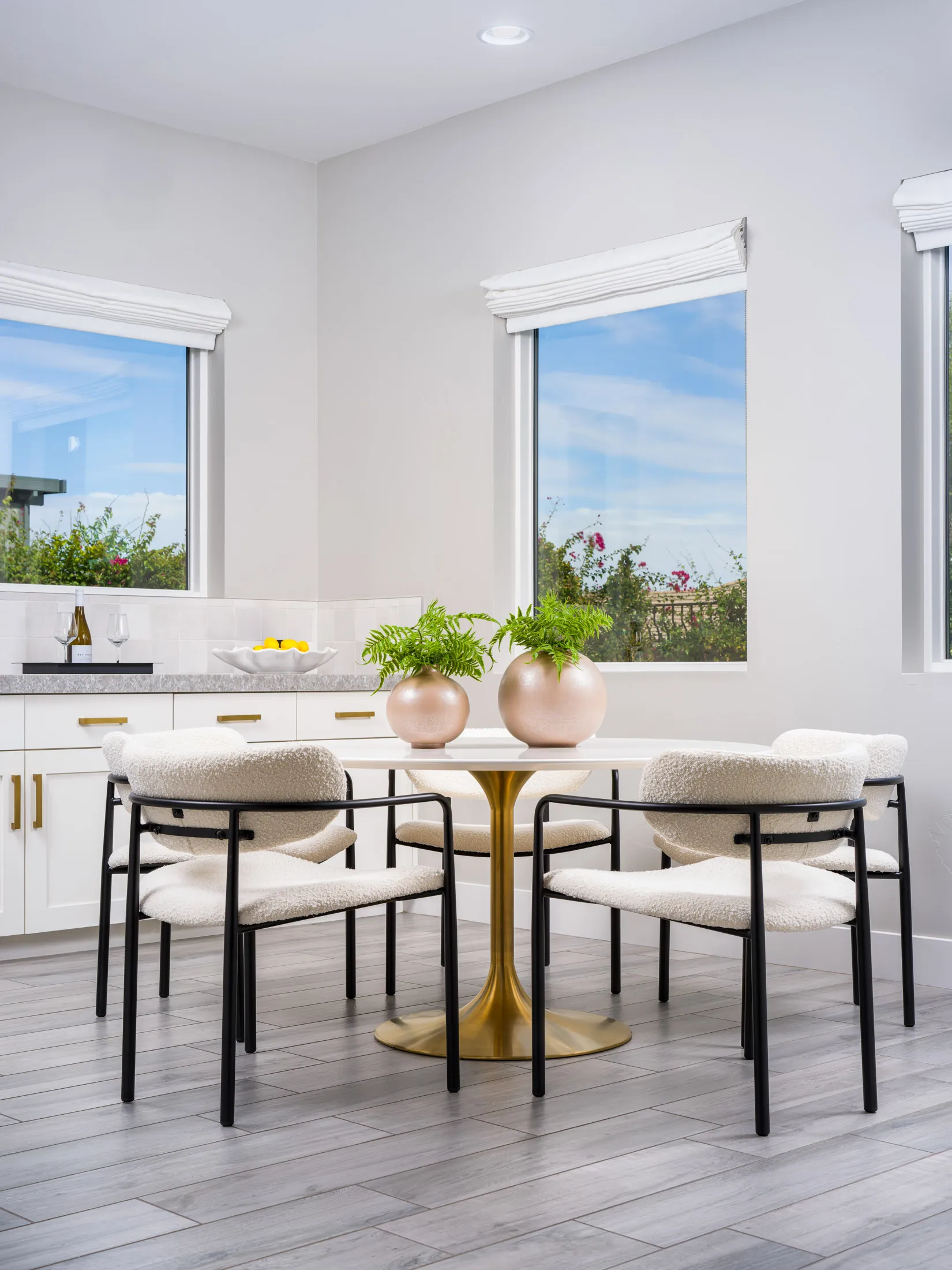 Bright dining area with a gold-base table, cream chairs, and greenery accents in a luxury staged home.