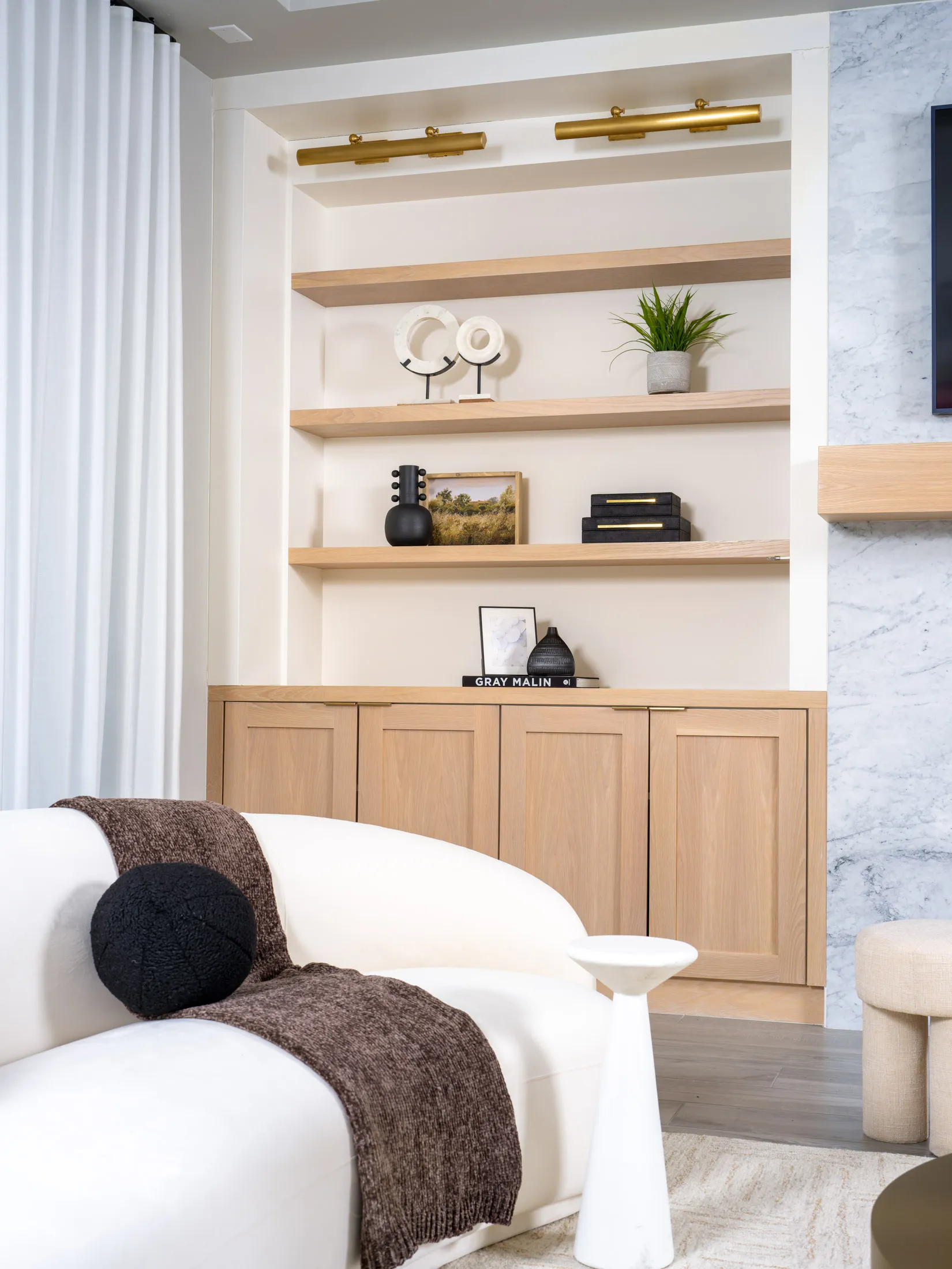 Sophisticated living room with custom wood shelving, gold lighting, neutral furniture, and modern decor accents in a luxury staged home.