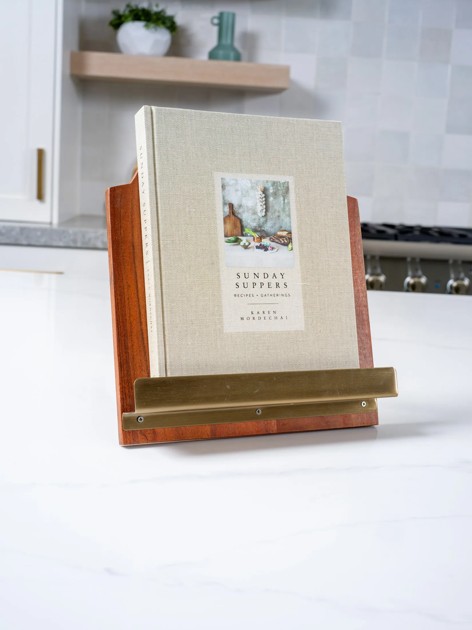 Hardcover cookbook on a wooden stand with brass accents staged in a modern luxury kitchen.