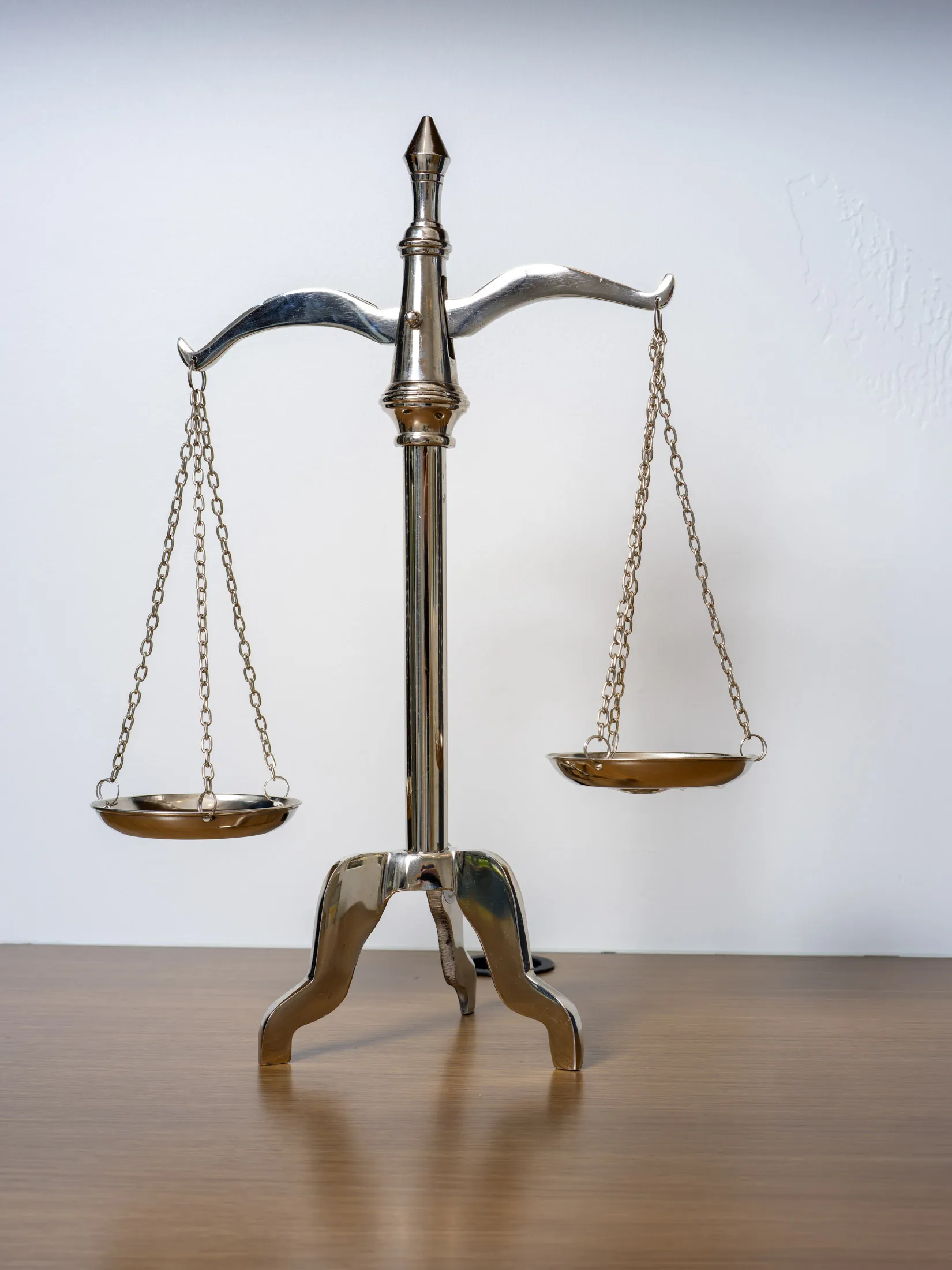 A decorative silver balance scale with intricate detailing, placed on a wooden surface against a neutral wall.
