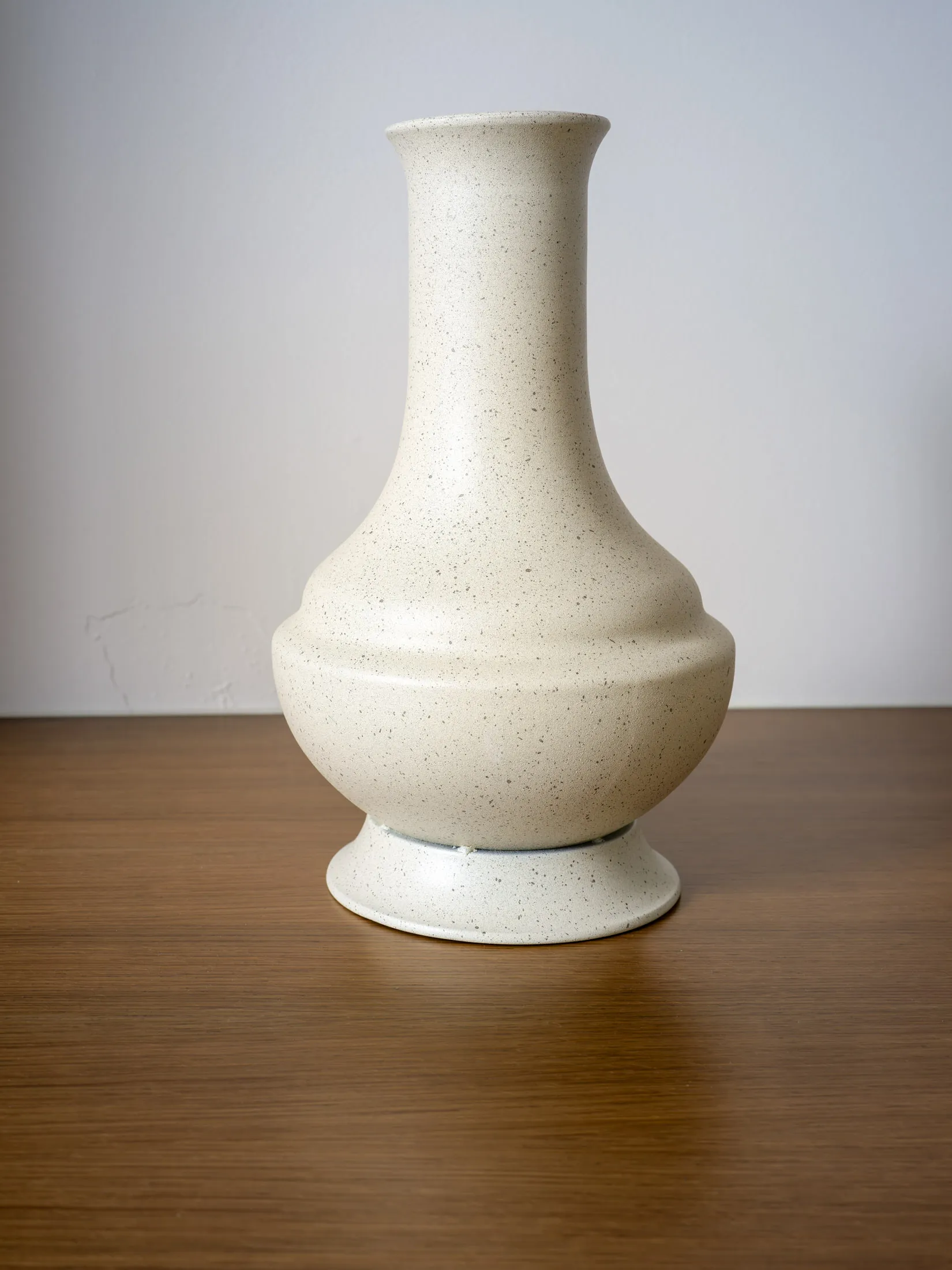 A minimalistic ivory ceramic vase with speckled texture, displayed on a wooden surface.