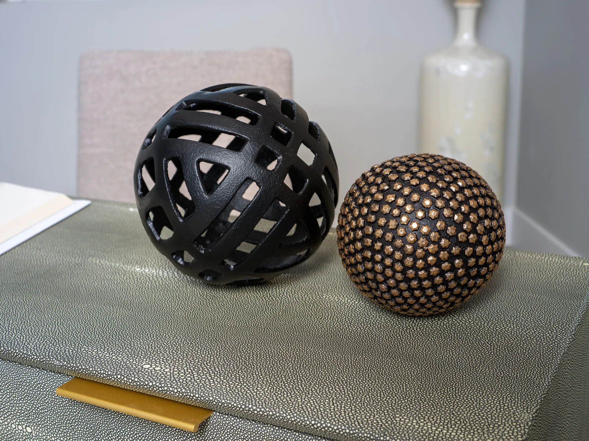 Two decorative orbs, one black with an open geometric design and the other with a textured gold and black pattern, placed on a textured console.