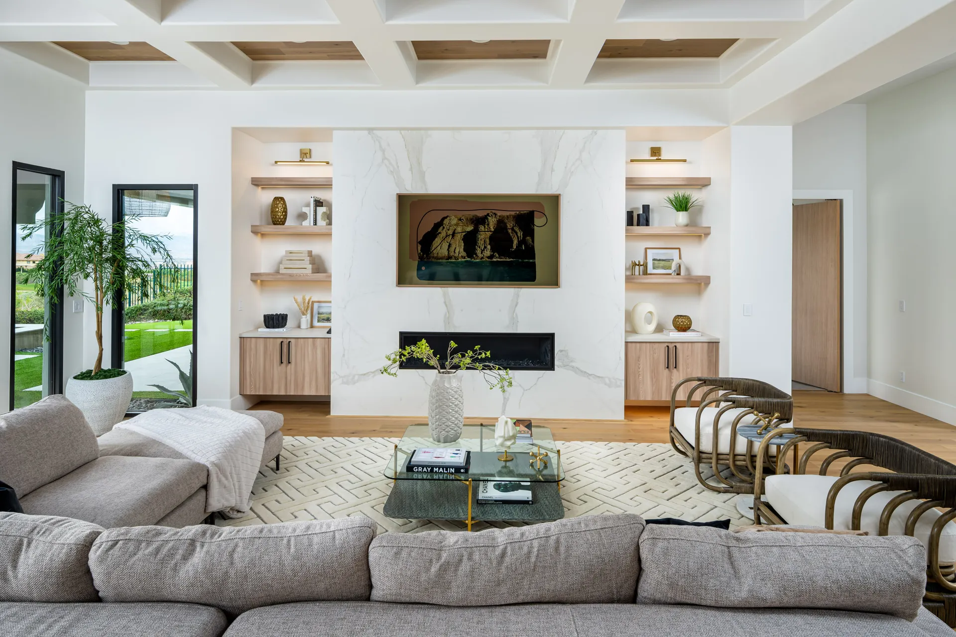 A living room centered around a large marble fireplace with built-in shelves, a gray sectional, and a glass coffee table.