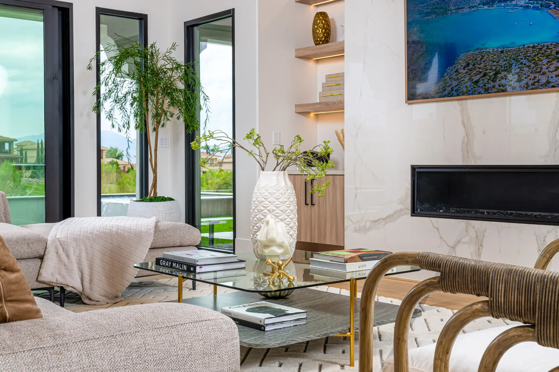 A seating area with a white textured vase on a glass coffee table, branches adding a fresh accent, and tall windows in the background.