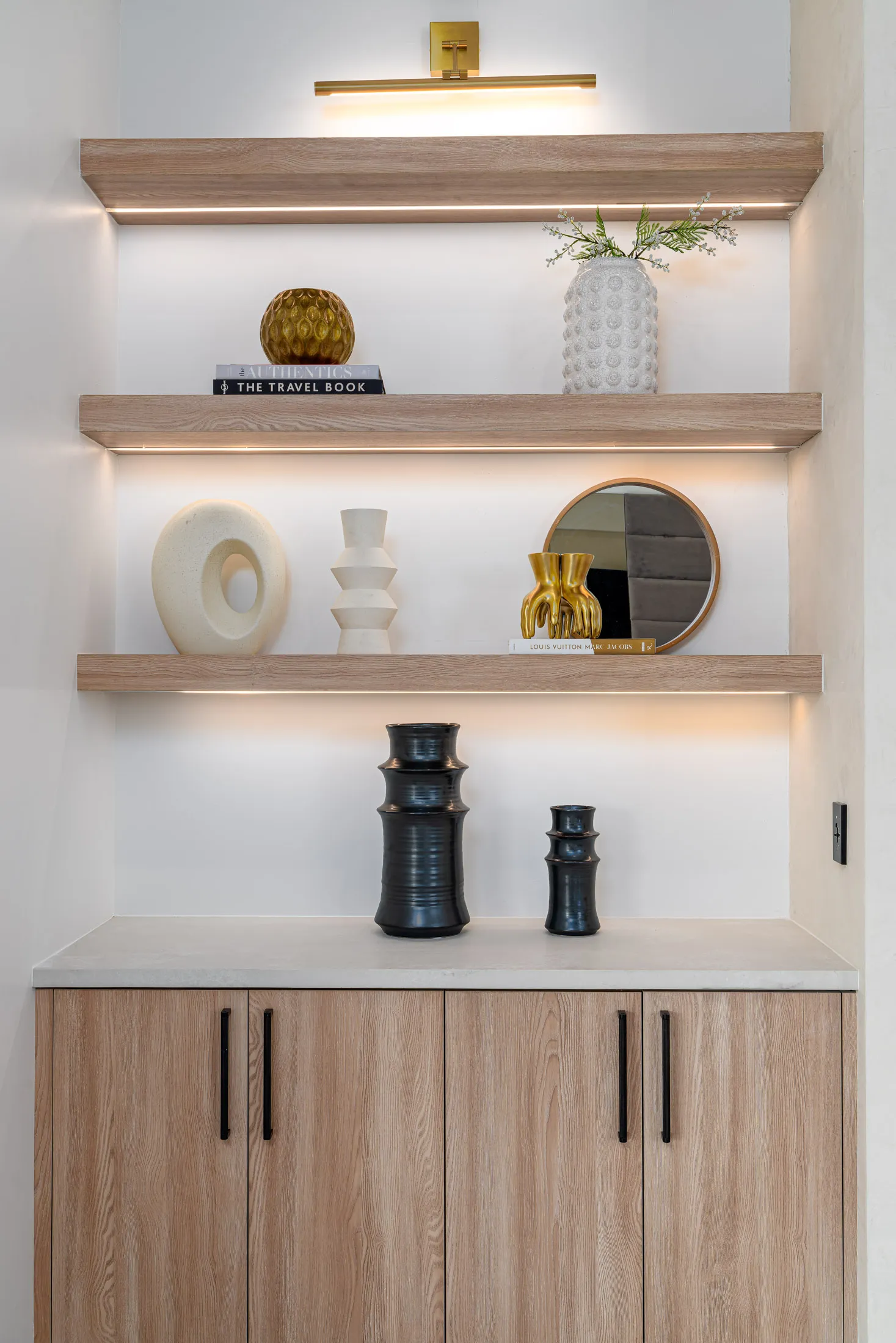 Open wood shelves showcasing various decorative vases, a mirror, and a brass picture light overhead.