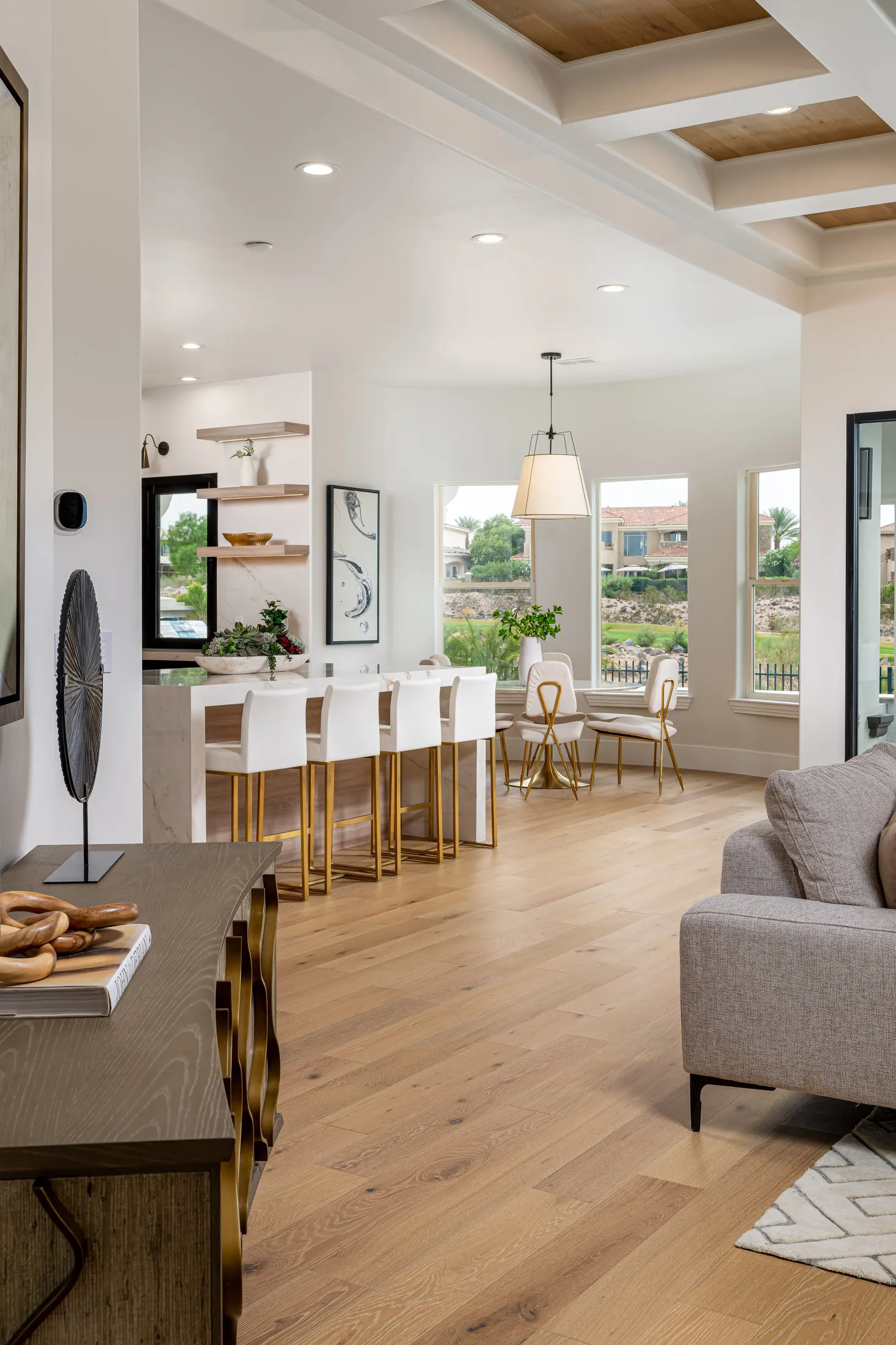 An open-concept space with a large marble island, gold-accented bar stools, and a bright dining nook near tall windows.