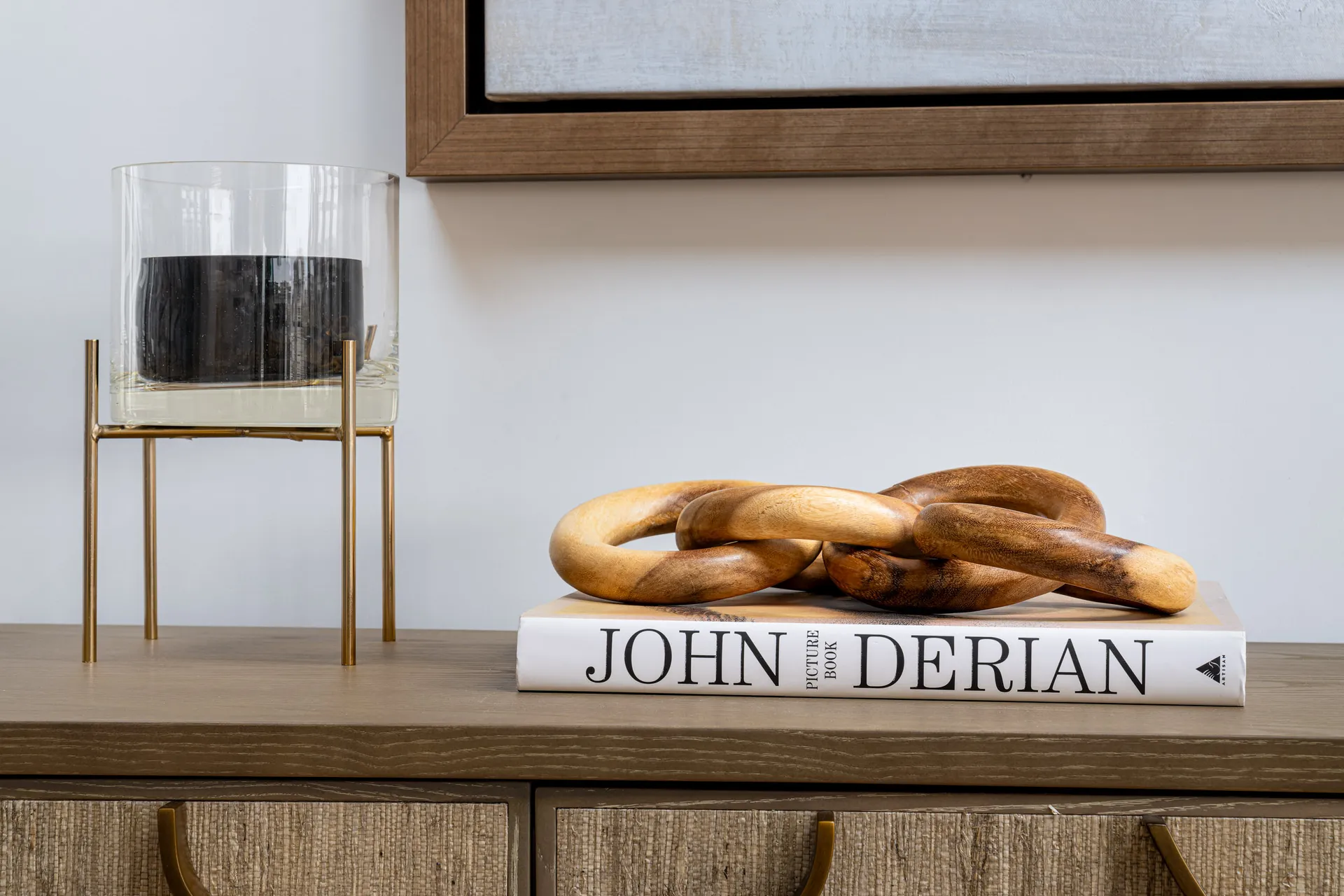 A wooden chain sculpture placed on a book, next to a glass candle holder on a slender gold stand.