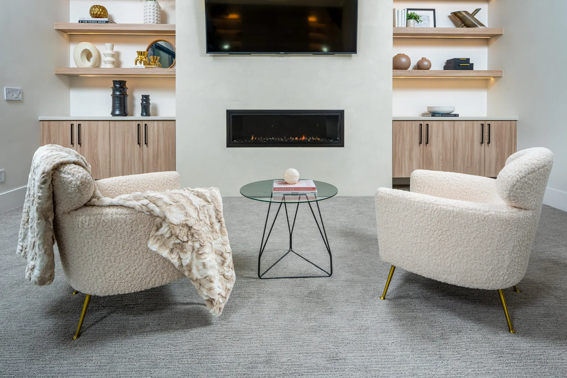 Two plush, round-back chairs face a wall-mounted fireplace, flanked by built-in cabinets and floating shelves.