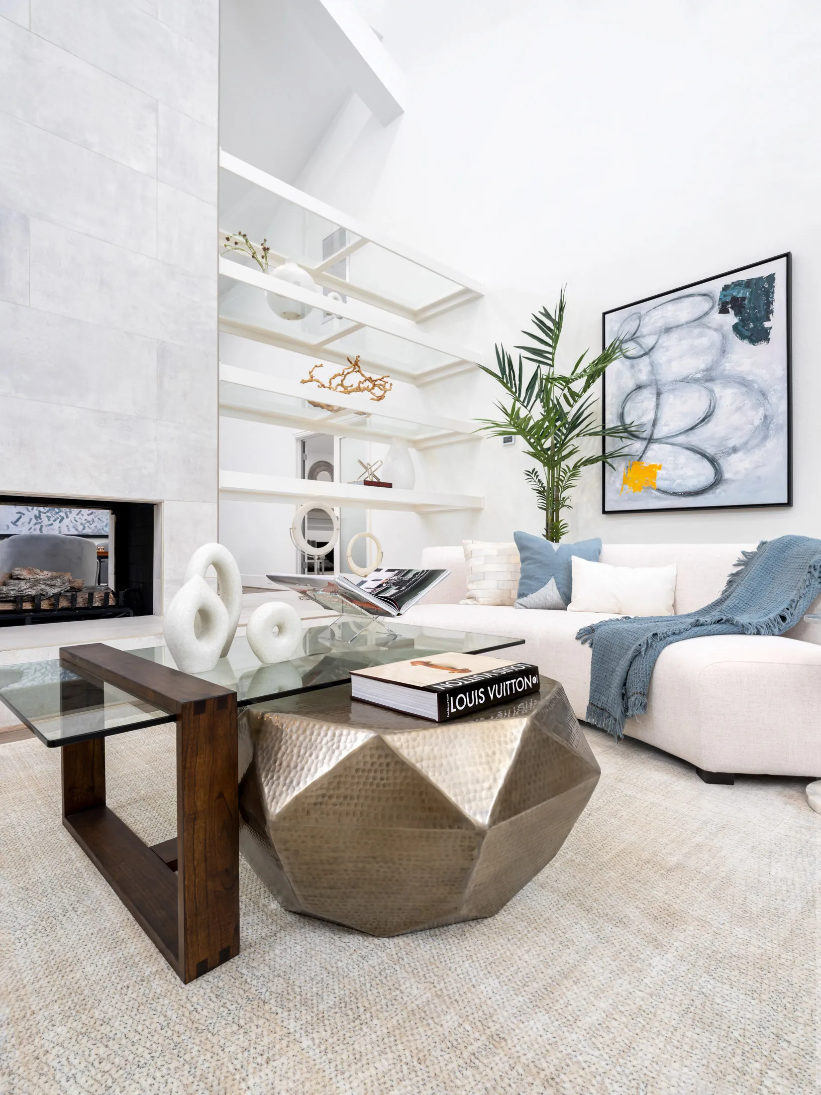 High-End Home Staging featuring a hammered metallic coffee table, layered glass surfaces, and an abstract painting on a white wall.