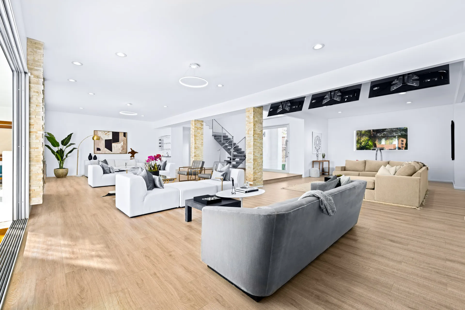 A spacious open living area featuring sofas in neutral tones, stone columns, and large sliding doors leading outside.