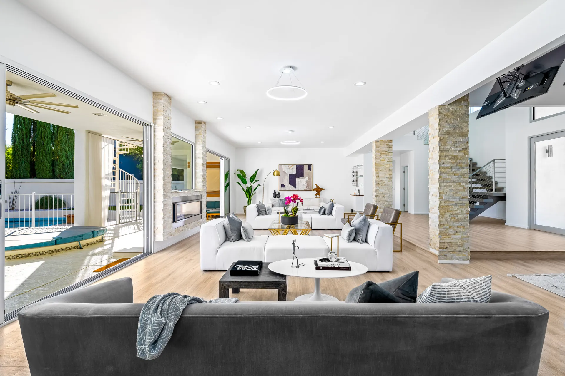 An open living area from a Las Vegas Home Staging project, showcasing white and gray seating, stone columns, and sliding doors leading to a pool and spiral staircase