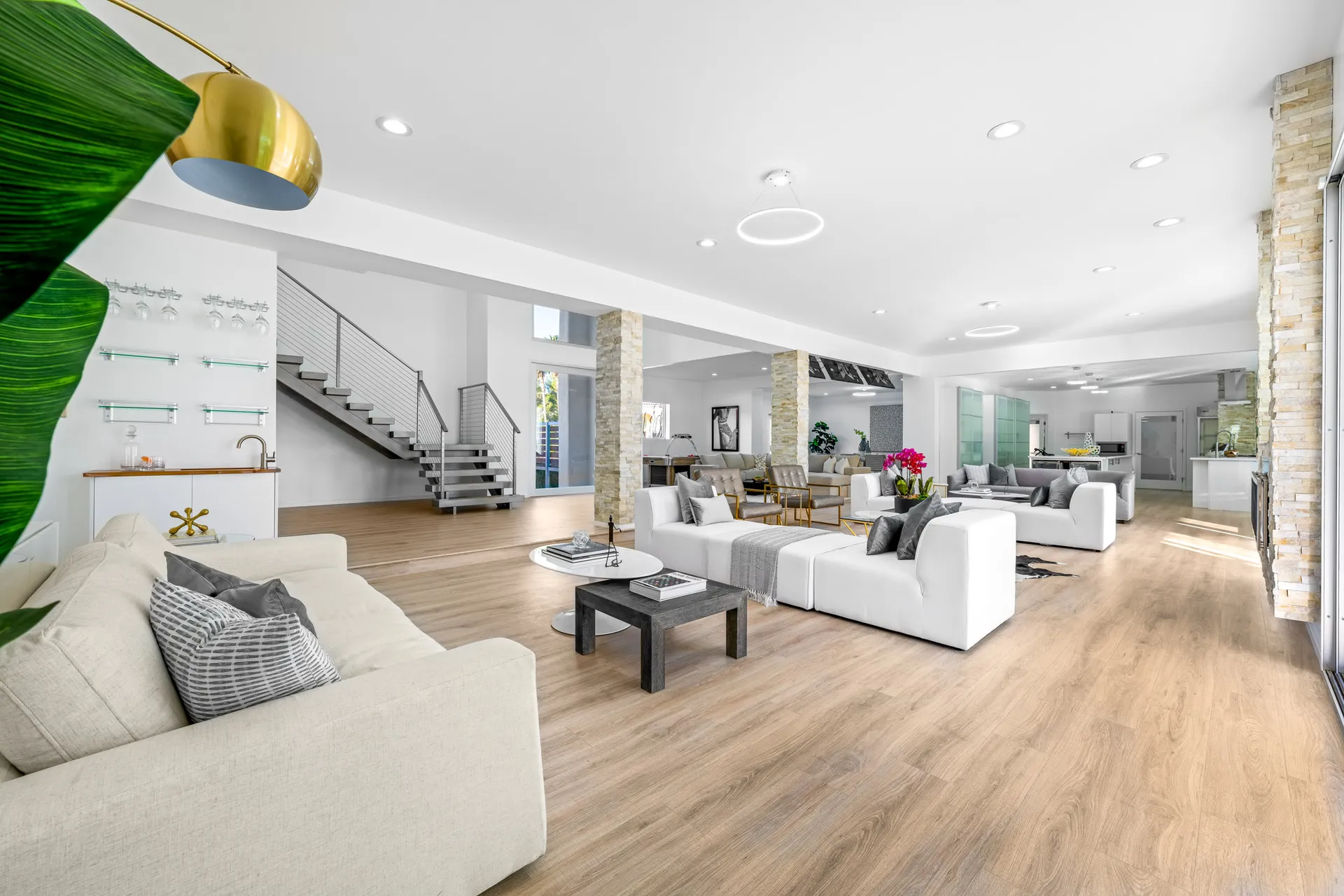 A wide, bright living area with white sofas, stone columns, and a modern metal staircase.