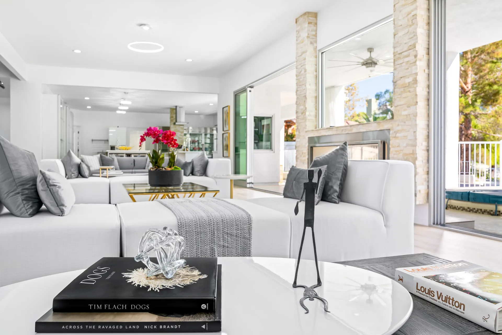 A white sectional in a bright living area, with pink orchids on a glass coffee table and large openings to the outside.