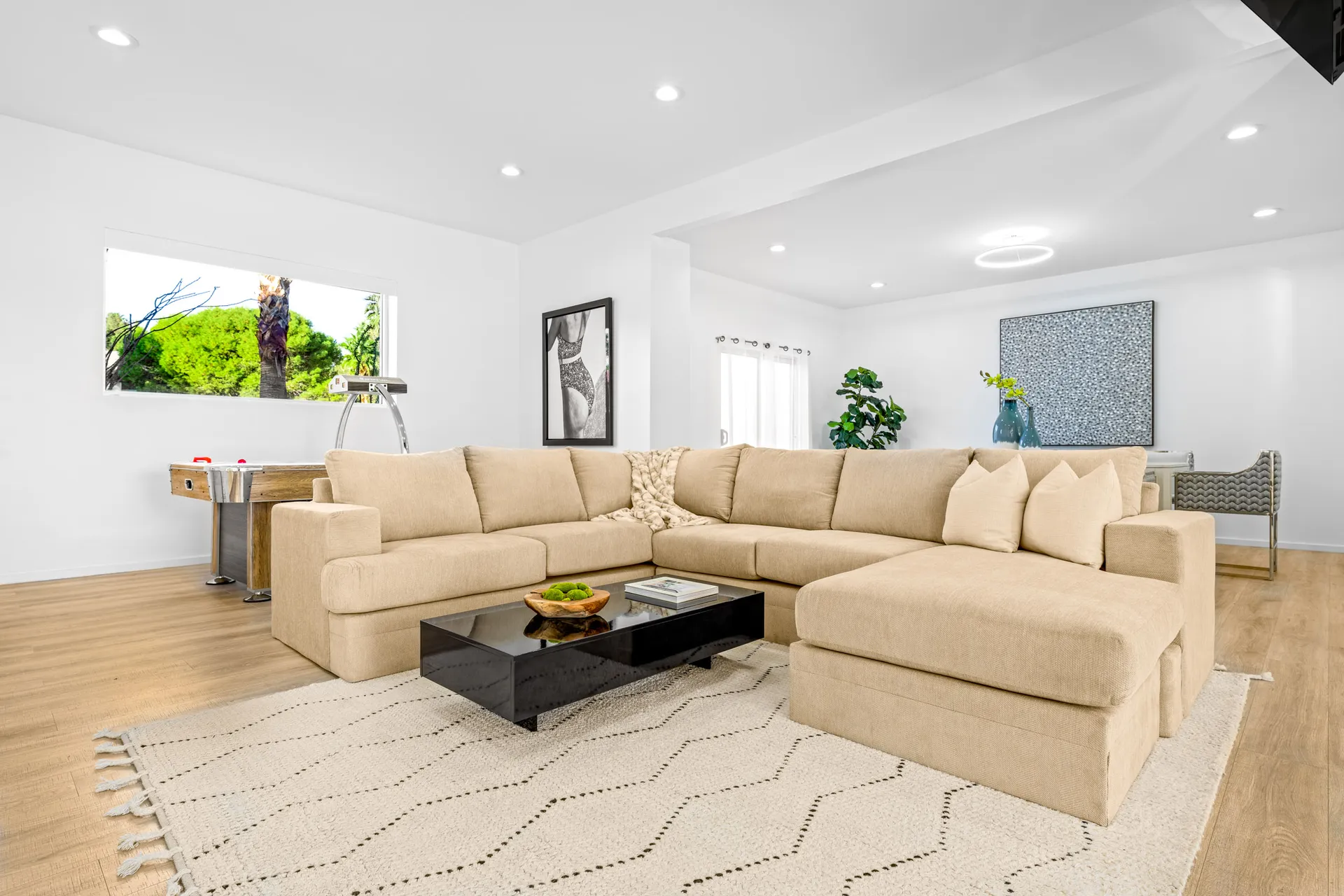 A spacious living area with a large beige sectional, a black coffee table, and an air hockey table.