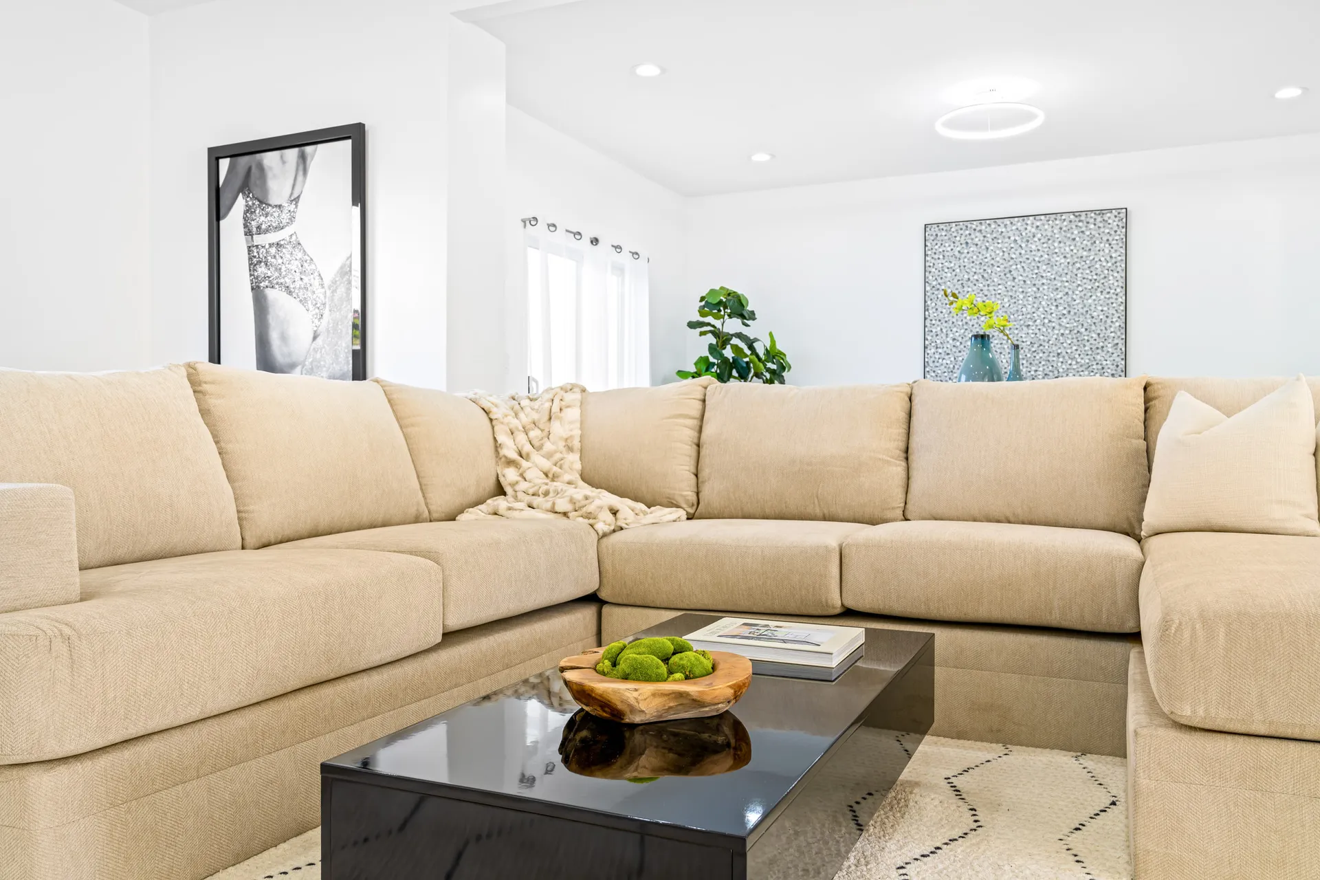 A large beige sectional sofa with a black coffee table holding a wooden bowl of green decor items.