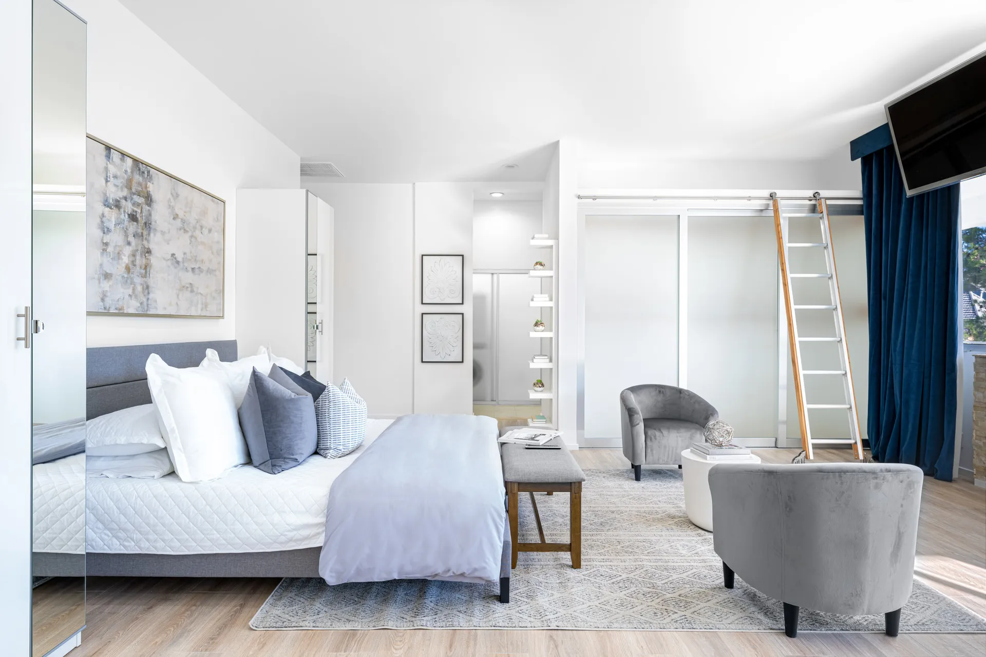 A contemporary bedroom with a gray bed, layered pillows, and a ladder near frosted sliding doors.