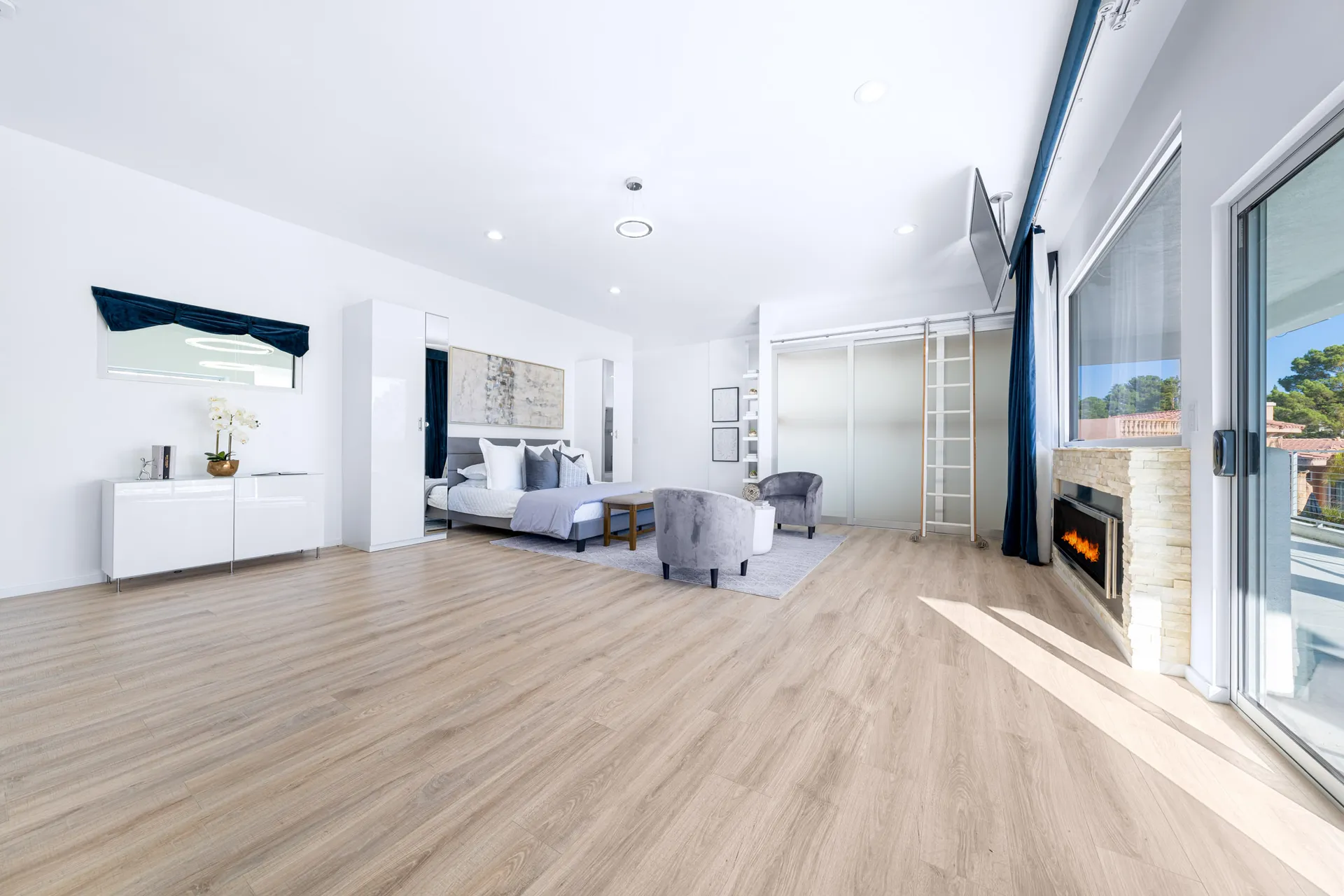 A bright, spacious bedroom with wood flooring, a fireplace, and modern furnishings.