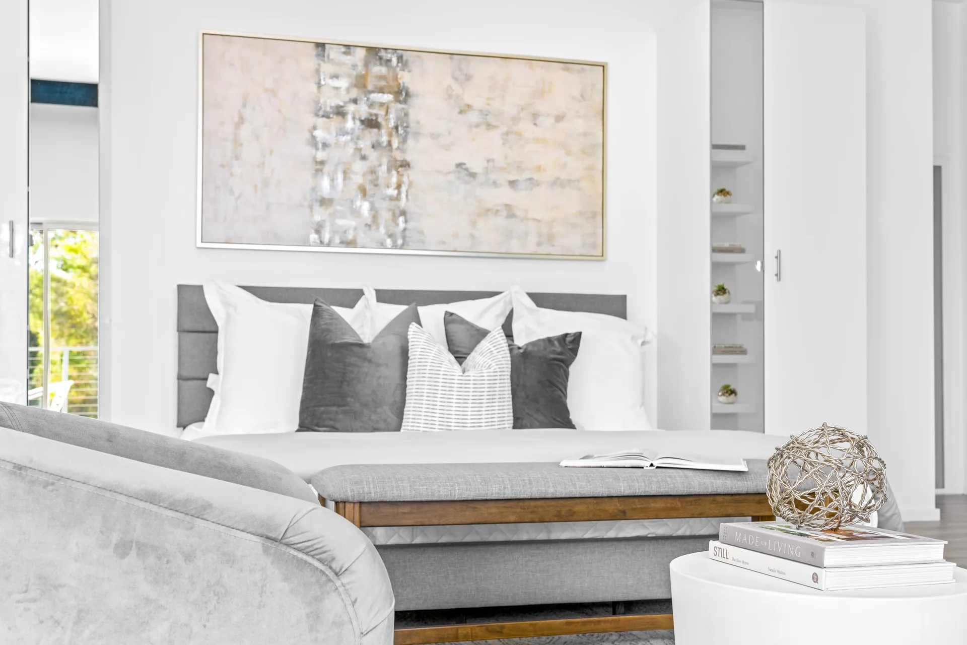 A sleek gray bed with layered pillows under a large abstract painting.