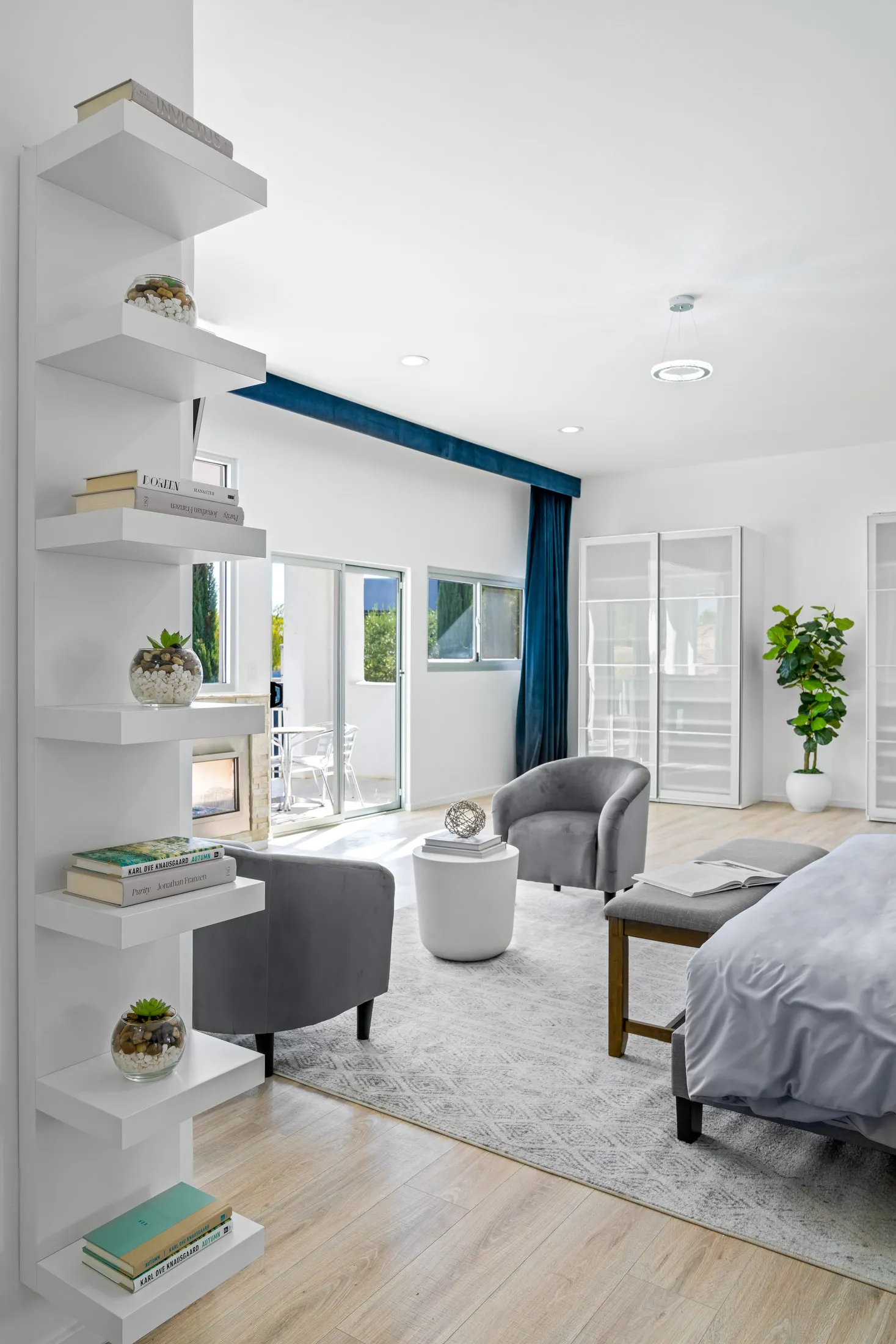 A bright bedroom suite with white shelving, gray chairs, and large windows leading to an outdoor space.