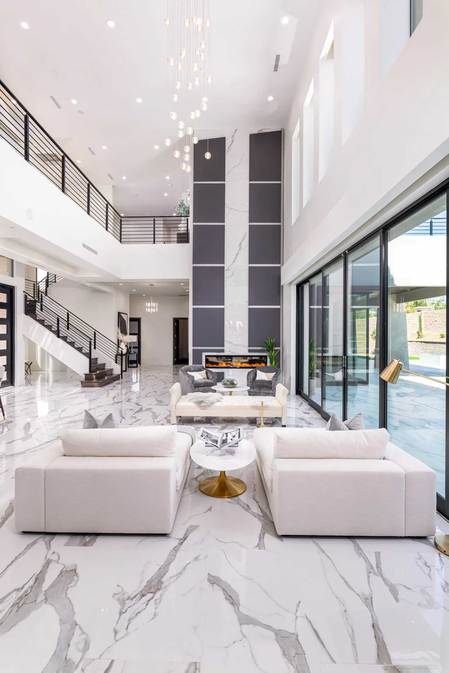 A spacious, modern living room with a white marble floor, high ceilings, and large windows. The room is furnished with white sofas, a glass coffee table, and a dining area. The space features a neutral color palette and a minimalist design, creating a luxurious and inviting atmosphere.