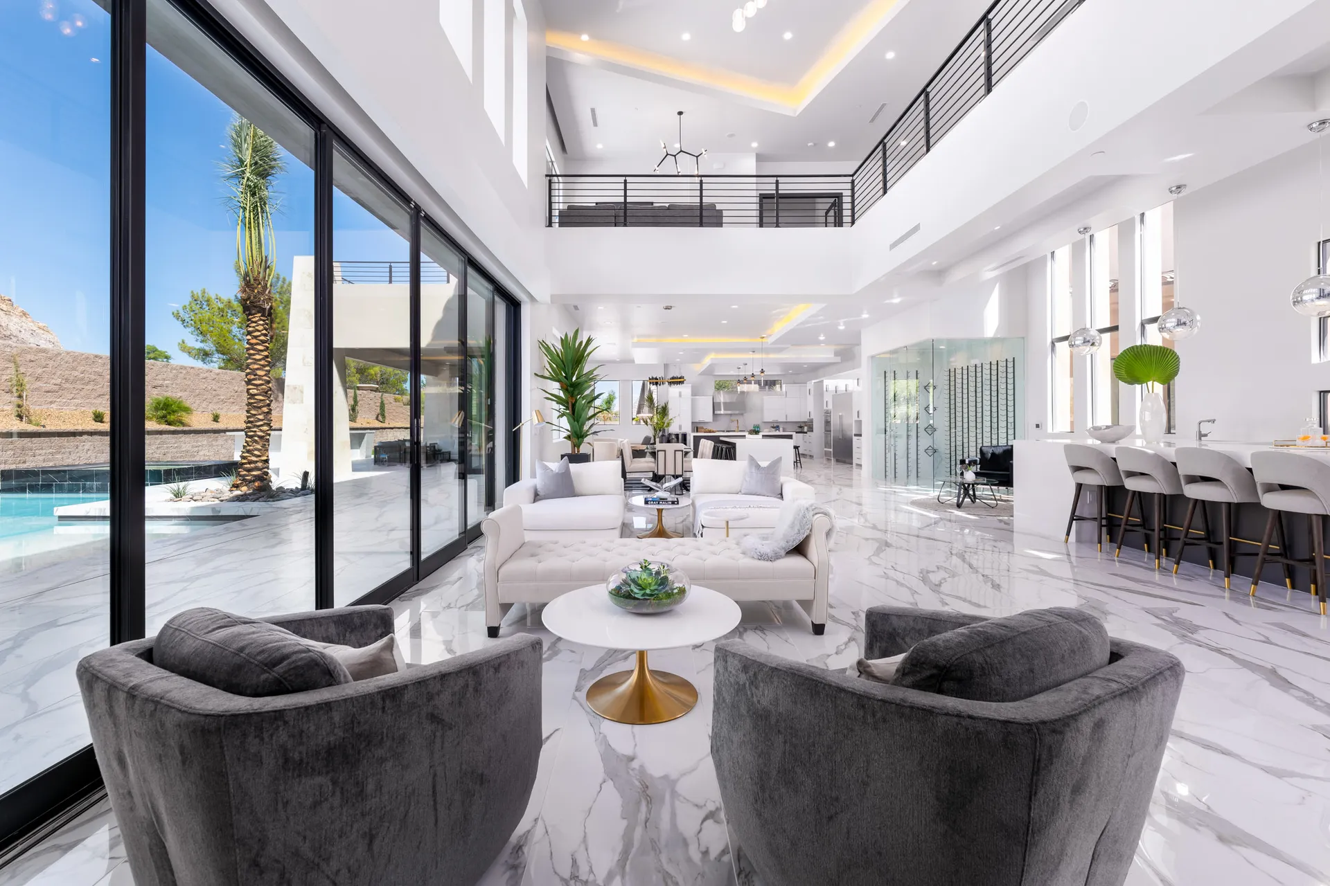 A spacious, modern living room with a white marble floor, high ceilings, and large windows. The room is furnished with white sofas, a glass coffee table, and a dining area. The space features a neutral color palette and a minimalist design, creating a luxurious and inviting atmosphere.