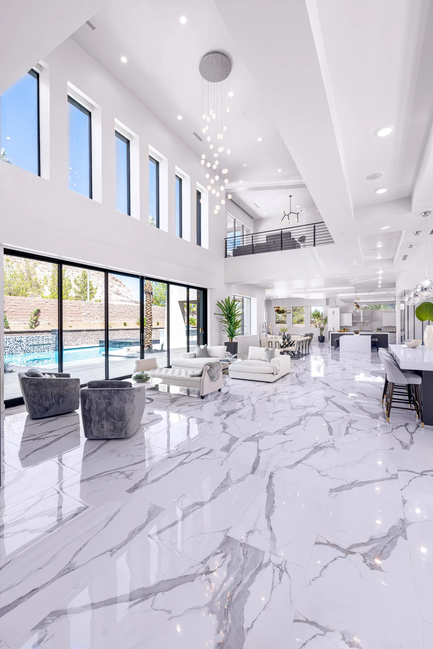 A spacious, modern living room with a white marble floor, high ceilings, and large windows. The room is furnished with white sofas, a glass coffee table, and a dining area. The space features a neutral color palette and a minimalist design, creating a luxurious and inviting atmosphere.