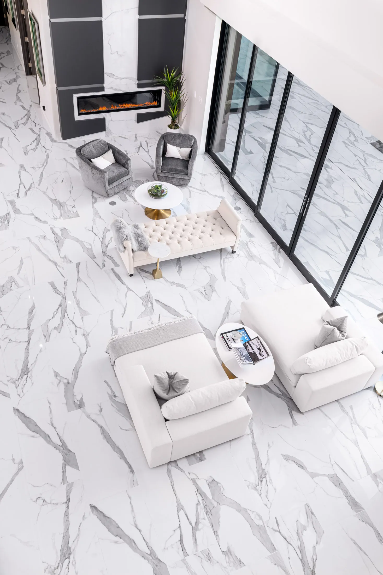 An overhead view of a modern living room with a white marble floor, a white sofa, and a fireplace. The room features a neutral color palette and a minimalist design, creating a serene and inviting atmosphere.
