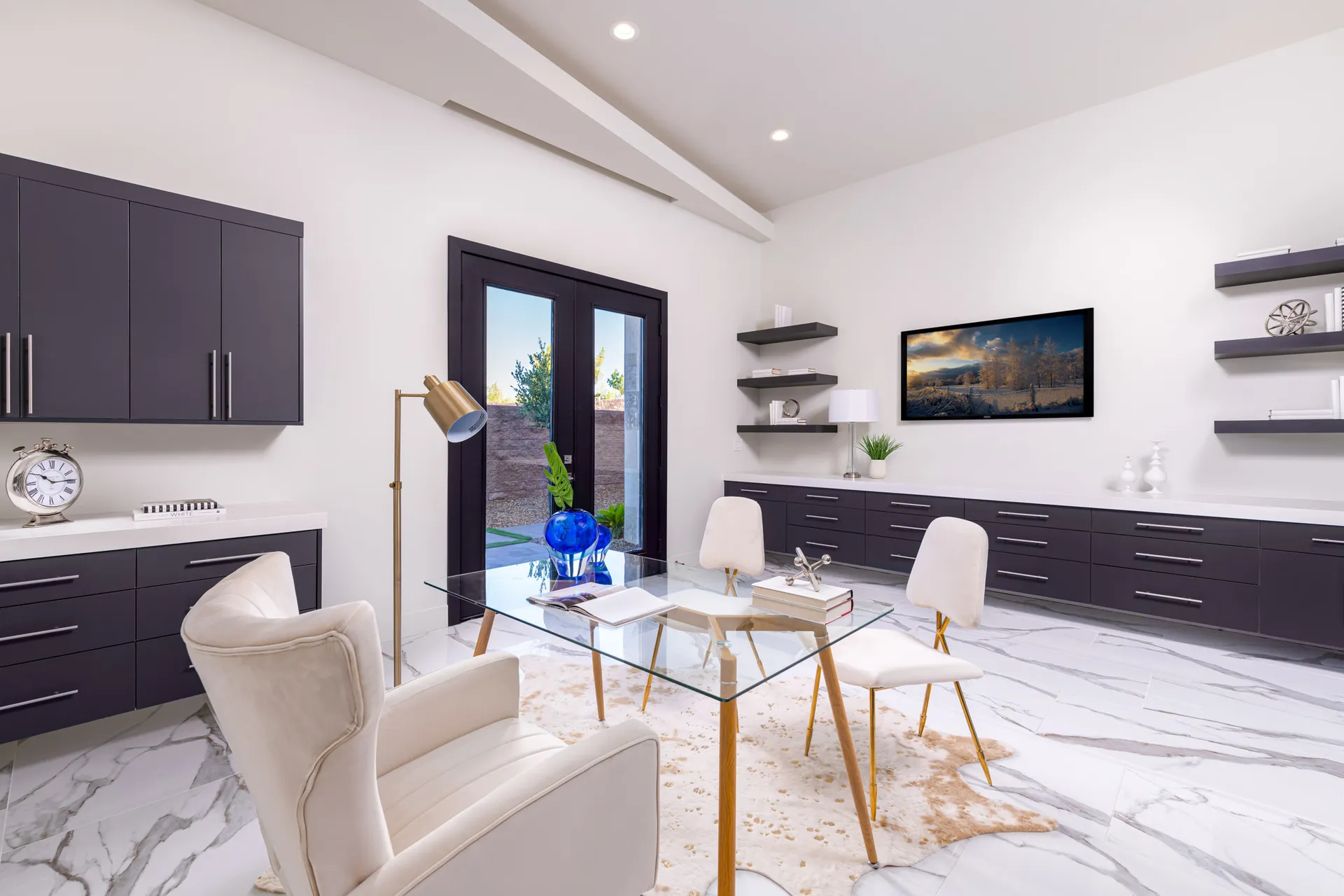 A home office with a glass desk, white chairs, a colorful artwork on the wall, and decorative objects on the desk. The design features a modern aesthetic with clean lines and a neutral color palette, creating a sophisticated and elegant look.