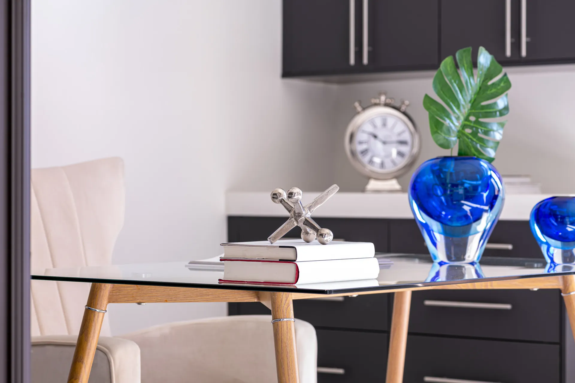 A close-up of a glass table with books, decorative objects, and blue vases. The design features a modern aesthetic with clean lines and a neutral color palette, creating a sophisticated and elegant look.