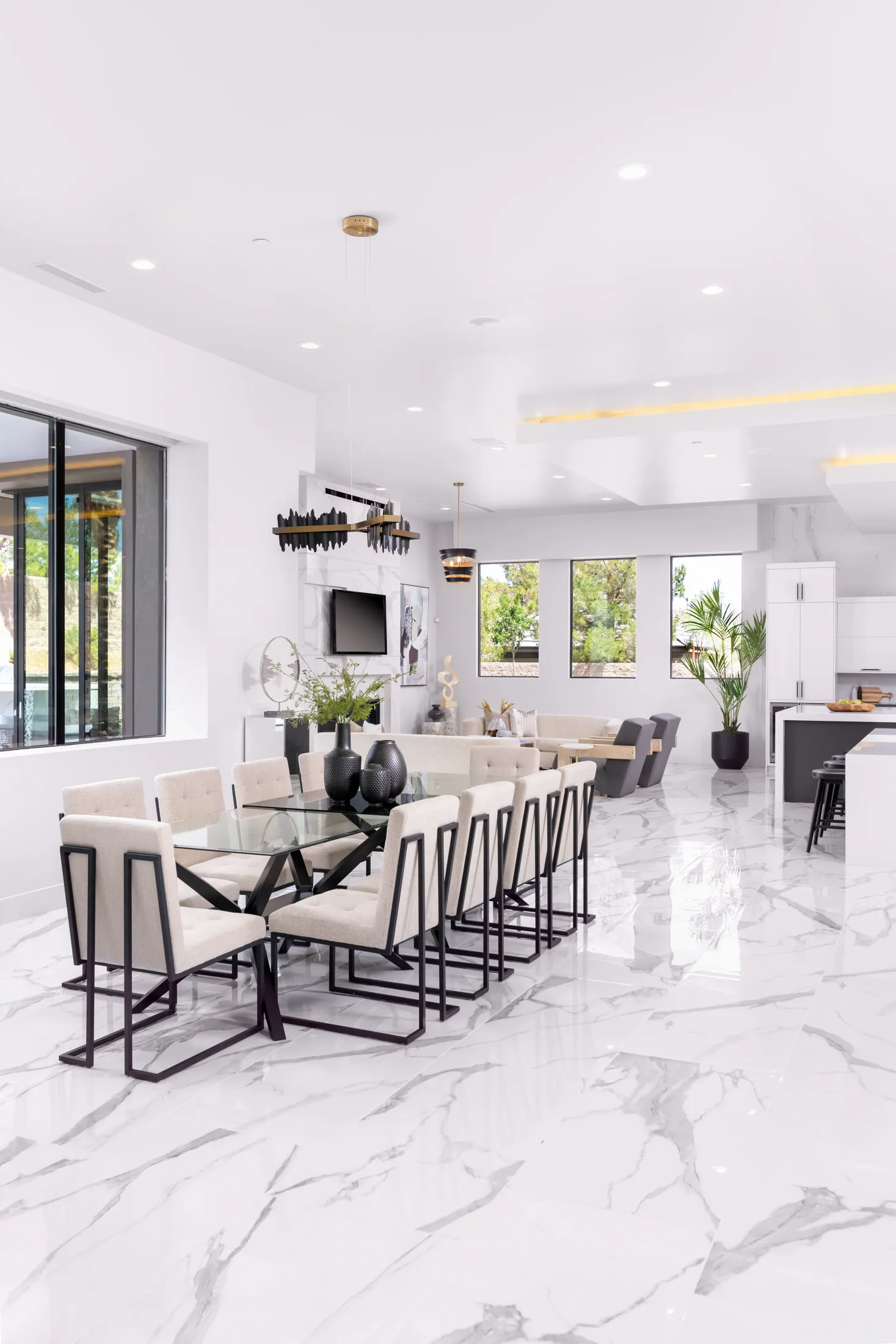 A dining room with a glass table, beige upholstered chairs, and decorative vases with greenery. The design features a modern aesthetic with clean lines and a neutral color palette, creating a sophisticated and elegant look.