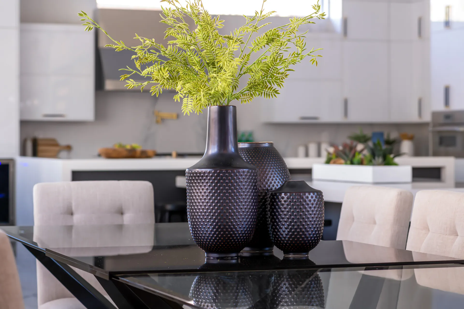 A close-up of a dining table with decorative vases and greenery, with a kitchen in the background. The design features a modern aesthetic with clean lines and a neutral color palette, creating a sophisticated and elegant look.