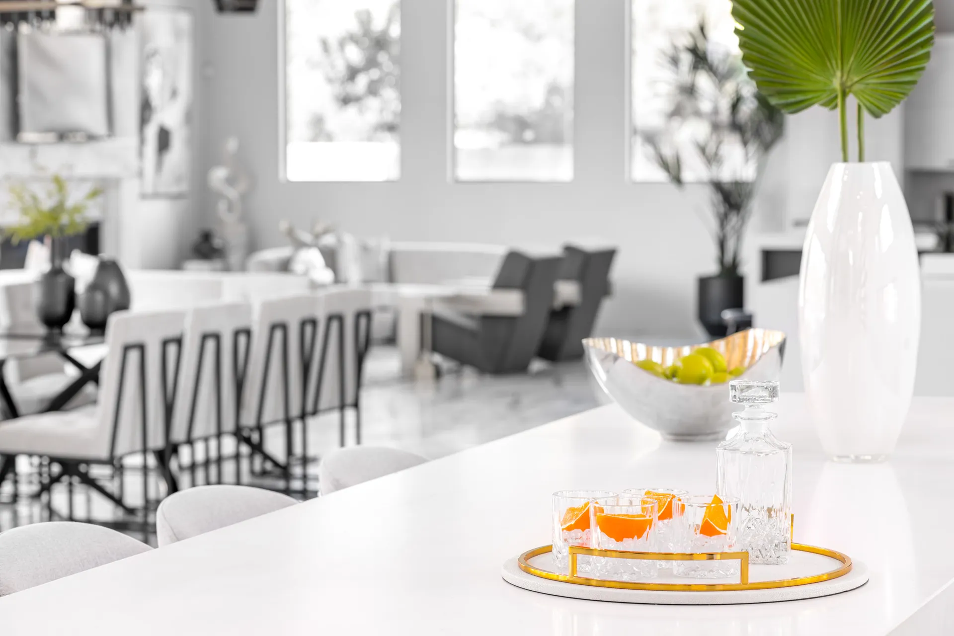 A bar area with a close-up of a tray with glasses and a pitcher on a white countertop. The background includes bar stools and a seating area, creating a stylish and functional space for entertaining.