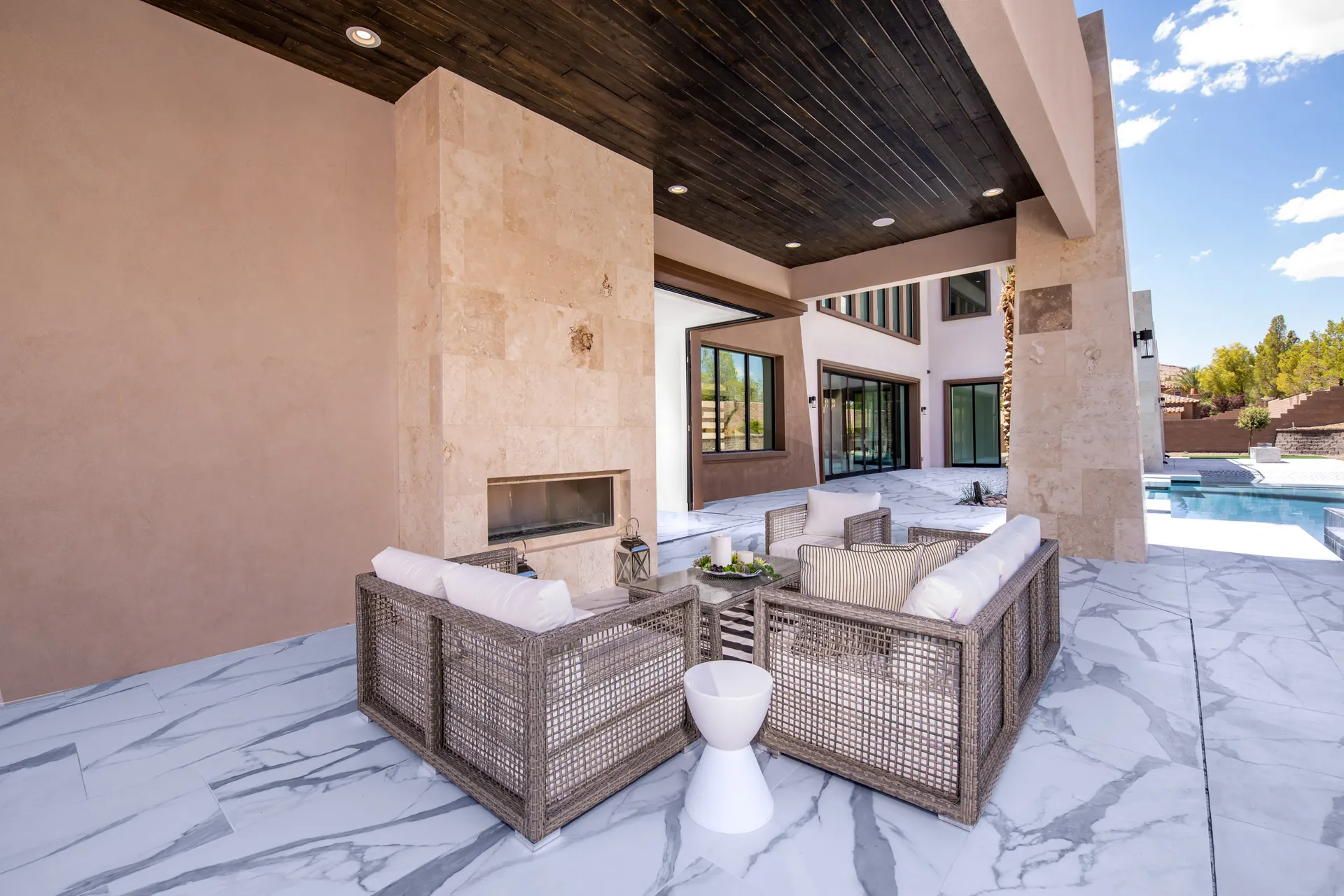 An outdoor seating area with wicker furniture, cushions, and a view of a pool and palm trees in the background. The arrangement features a comfortable and inviting setting, perfect for relaxation and outdoor gatherings.