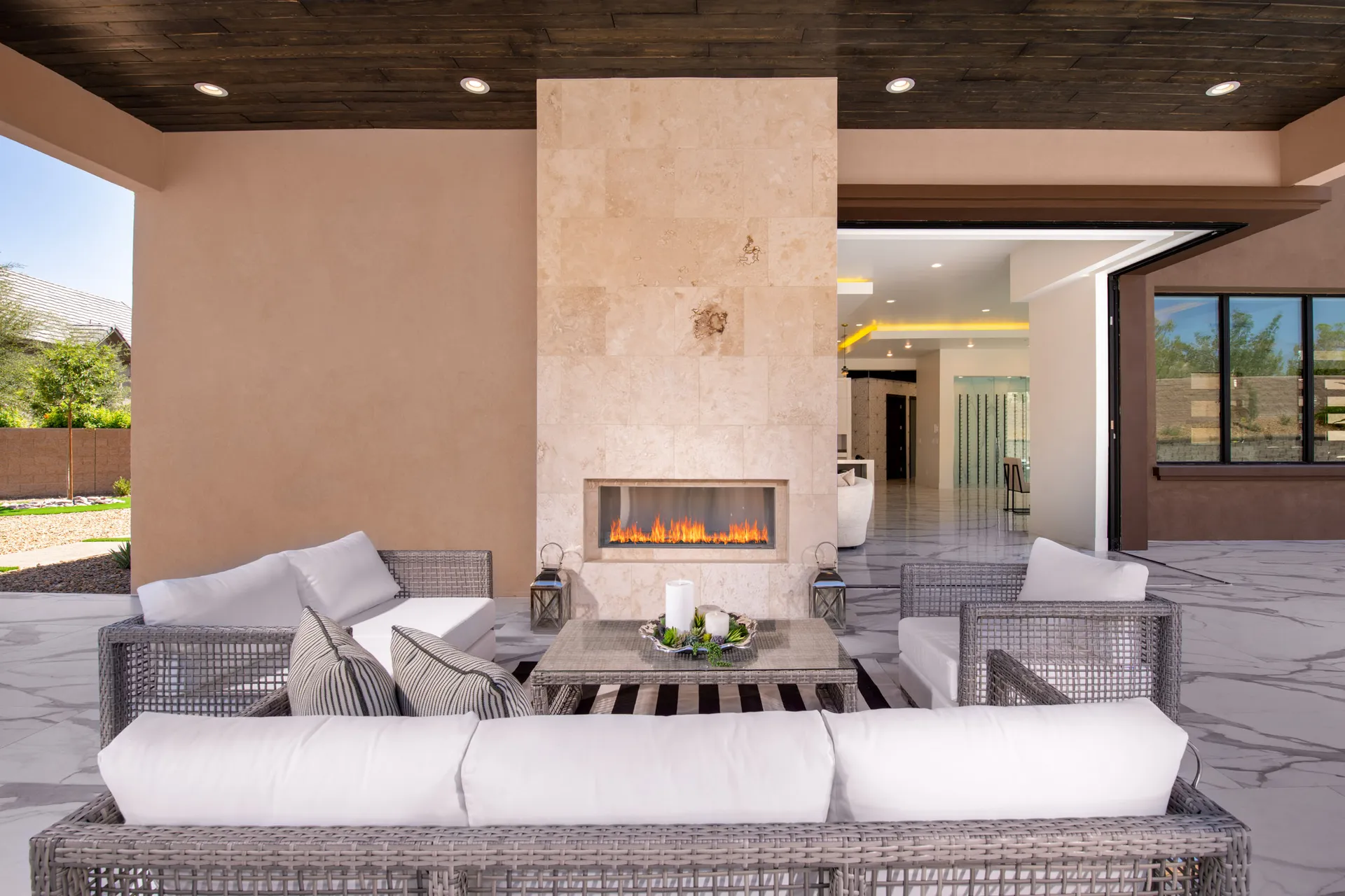 An outdoor patio with a large stone fireplace, wicker furniture, and a wooden ceiling. The arrangement features a comfortable and inviting setting, perfect for relaxation and outdoor gatherings.