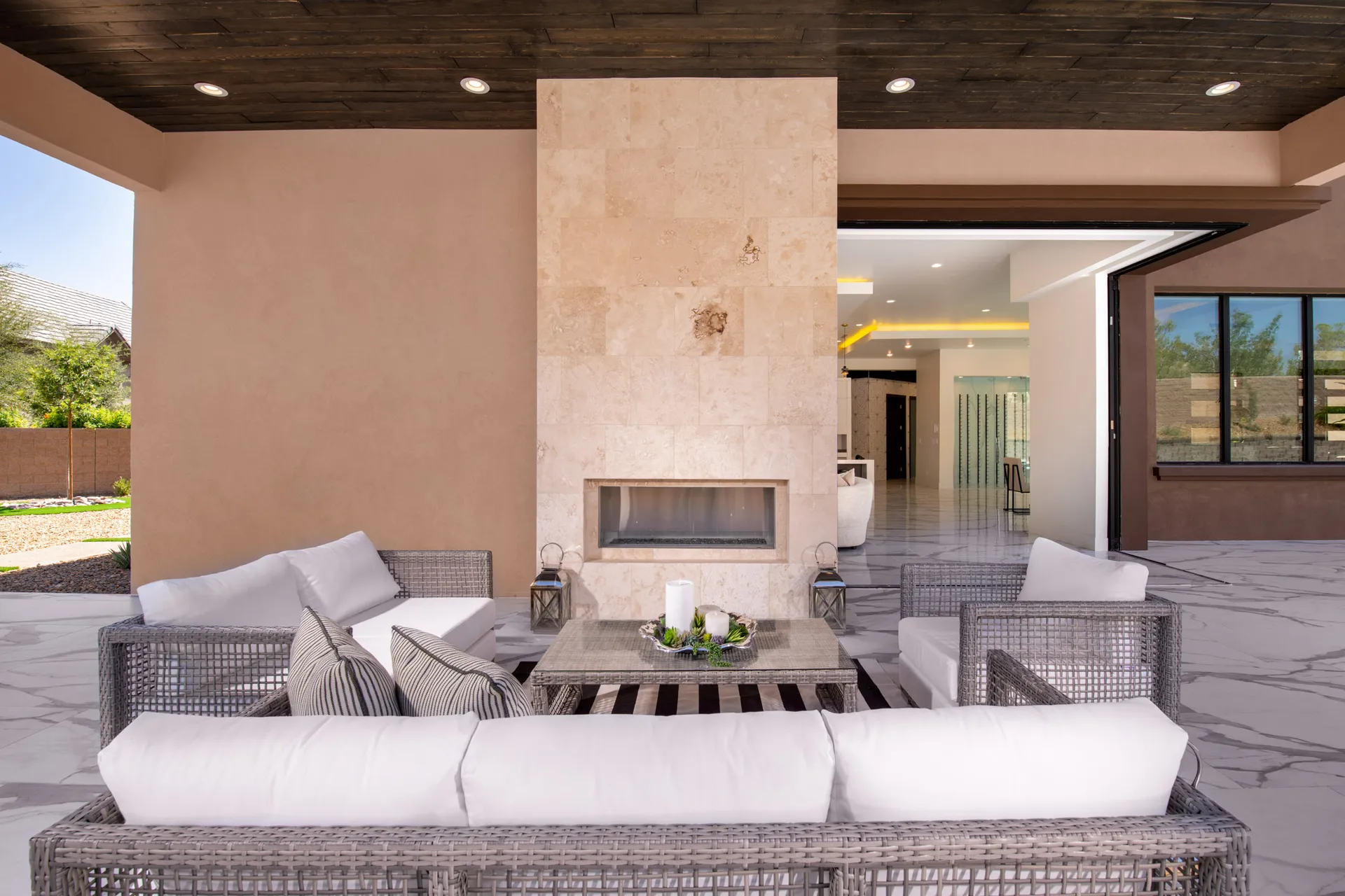 An outdoor seating area with wicker furniture, cushions, and a stone fireplace. The arrangement features a comfortable and inviting setting, perfect for relaxation and outdoor gatherings.