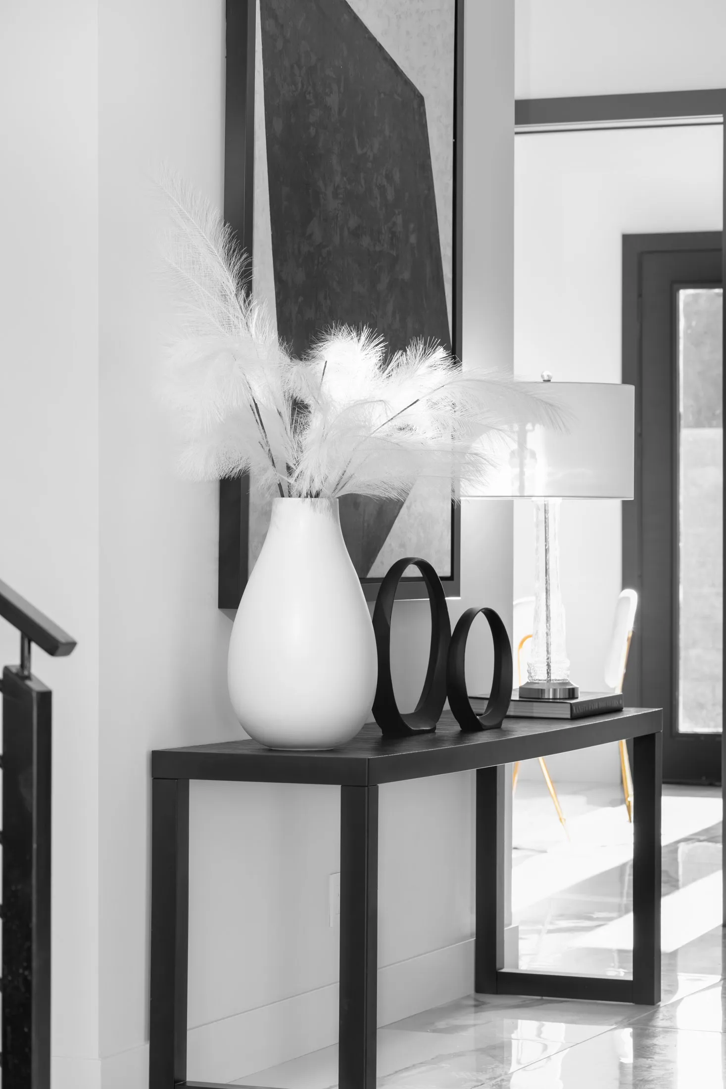 A hallway with a decorative console table, a large vase with pampas grass, and a table lamp. The design features a minimalist aesthetic with clean lines and a neutral color palette, creating a serene and elegant atmosphere.