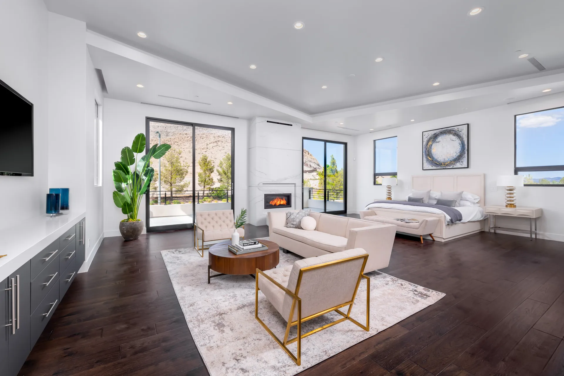 A spacious bedroom with a seating area, a bed, and large windows offering a view of the outdoors. The design features a modern aesthetic with clean lines and a neutral color palette, creating a serene and inviting atmosphere.