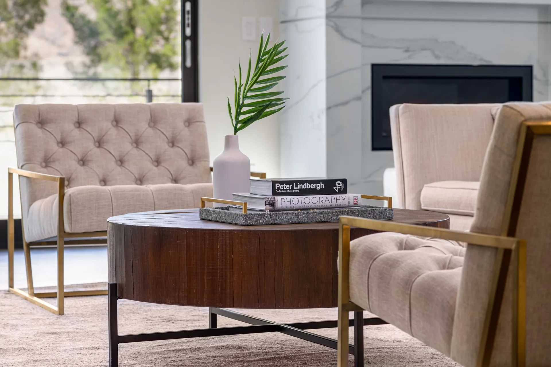 A seating area with tufted chairs, a wooden coffee table, and a vase with green foliage. The design features a modern aesthetic with clean lines and a neutral color palette, creating a sophisticated and inviting atmosphere.