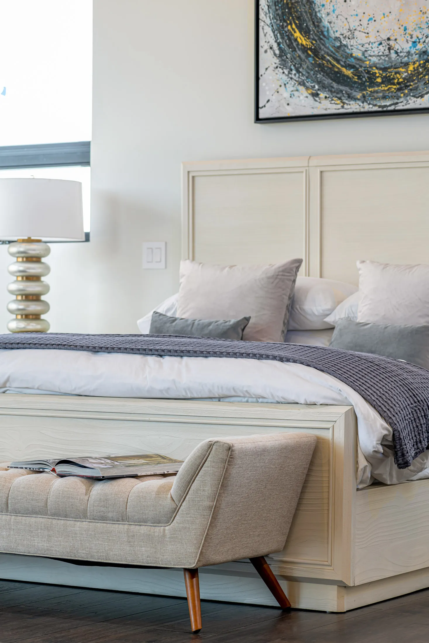 A master bedroom with a bed, a tufted bench, and a large abstract painting on the wall. The design features a modern aesthetic with clean lines and a neutral color palette, creating a serene and elegant atmosphere.