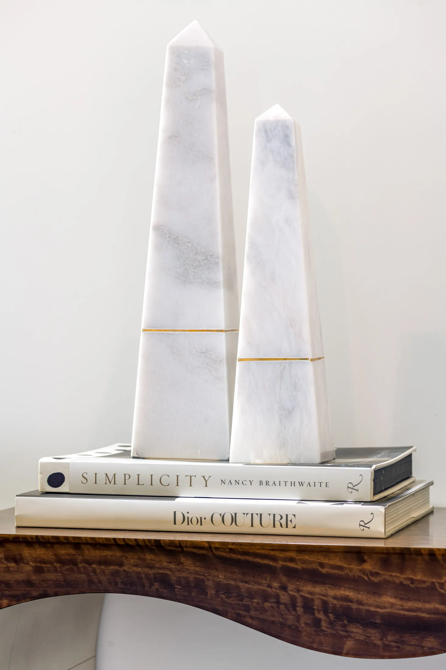 A decorative arrangement of books and marble obelisks on a wooden table. The design features a minimalist aesthetic with clean lines and a neutral color palette, creating a sophisticated and elegant look.