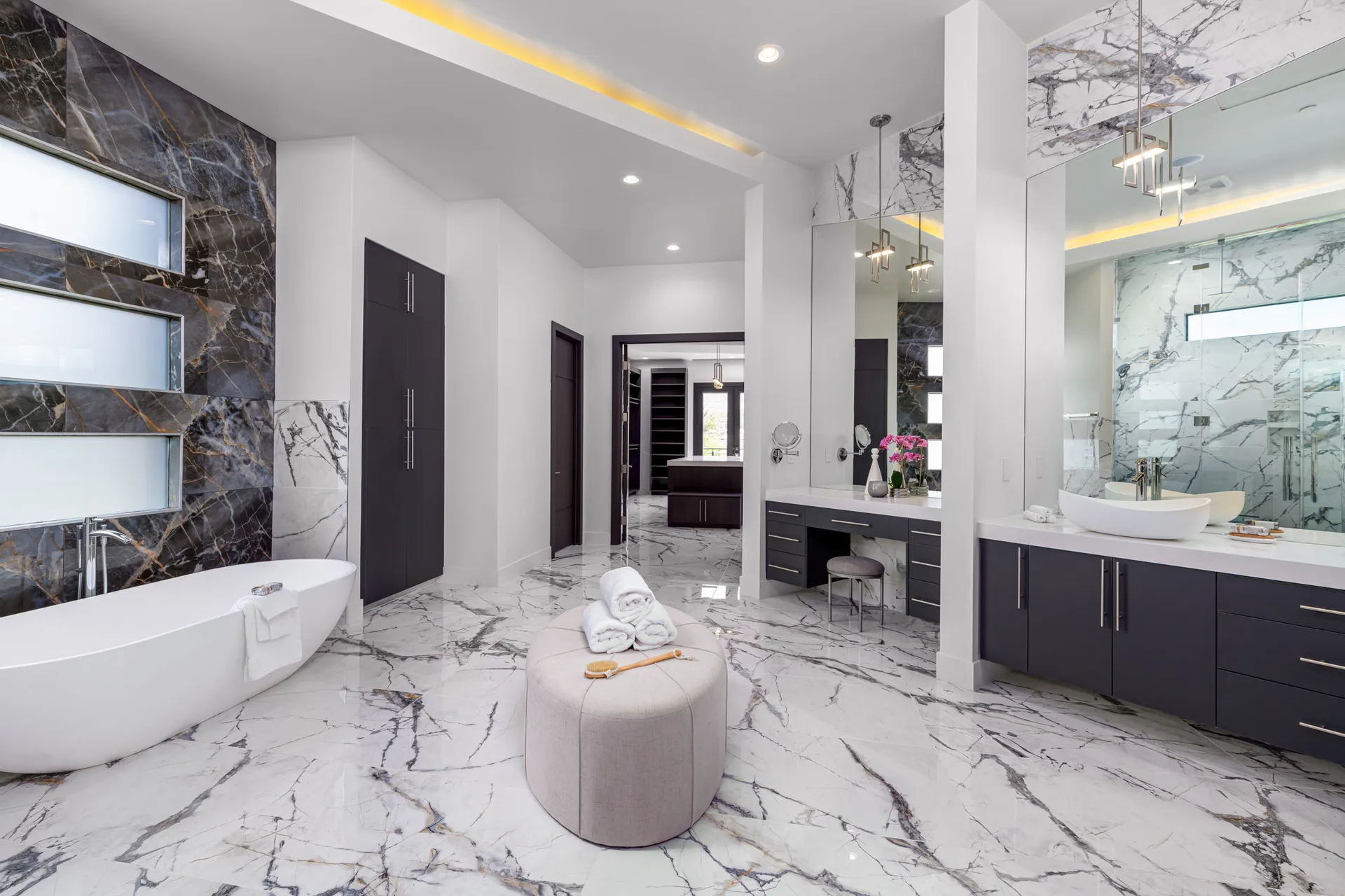 A luxurious bathroom with a marble floor, a freestanding bathtub, a double vanity with mirrors, and a seating area. The design features a modern aesthetic with clean lines and a neutral color palette, creating a serene and elegant atmosphere.