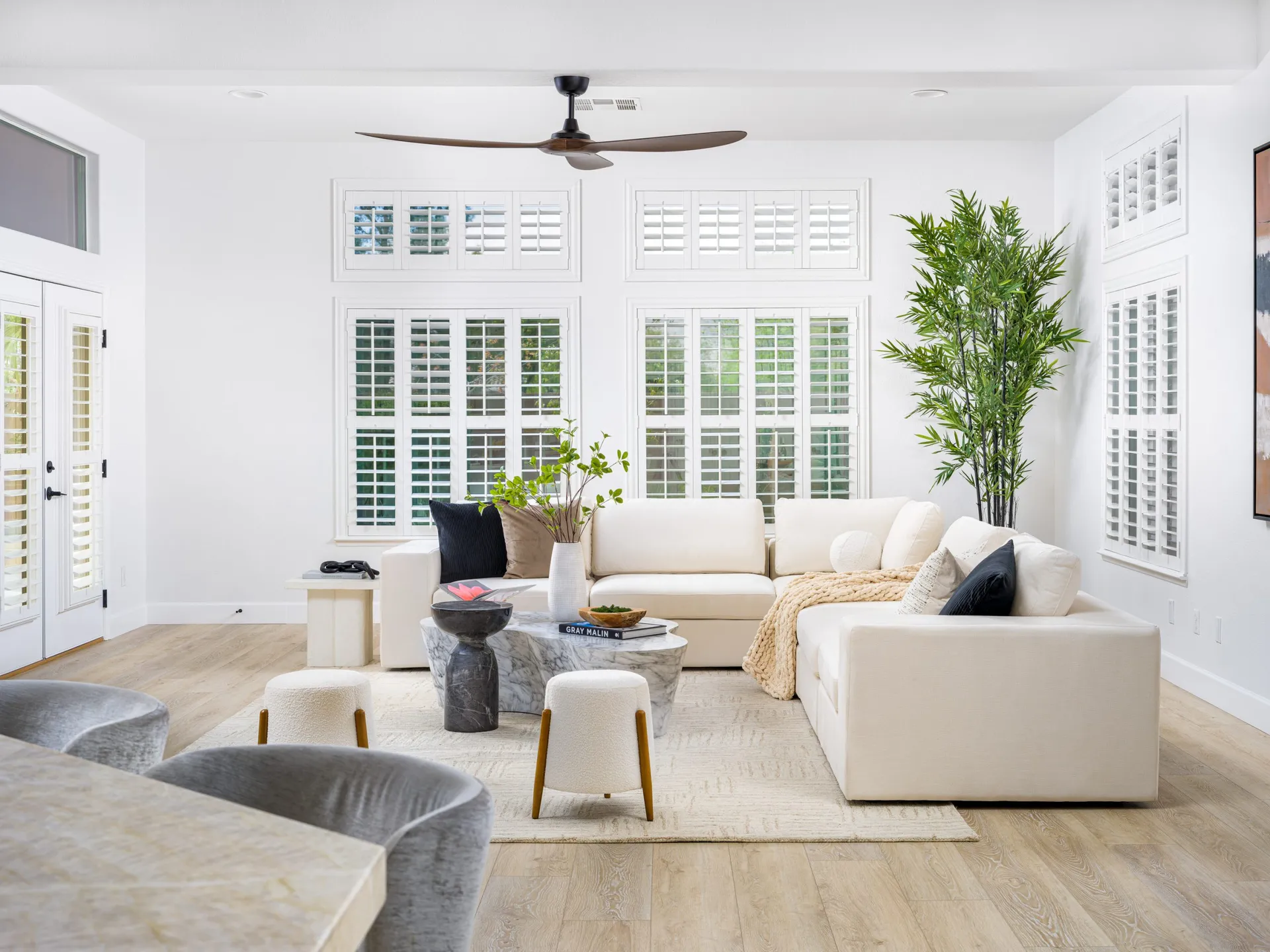 Spacious living room with white sofas, wooden coffee table, and large windows with shutters