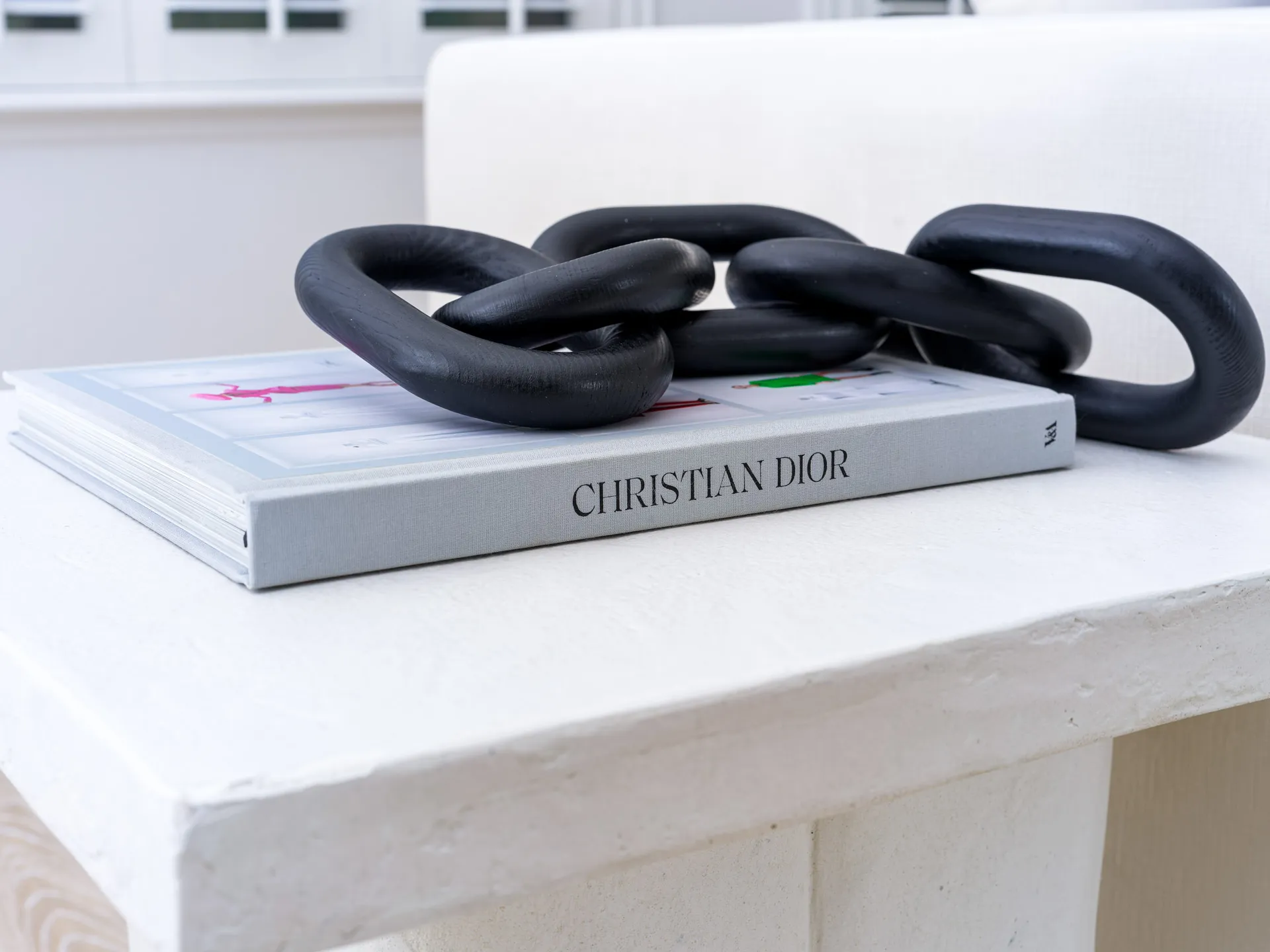 A black chain sculpture placed on top of a Christian Dior coffee table book.