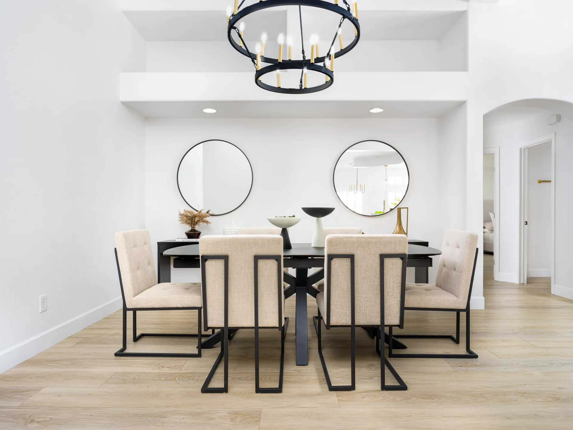 A contemporary dining area with a black table, neutral upholstered chairs featuring black metal frames, and round wall mirrors.