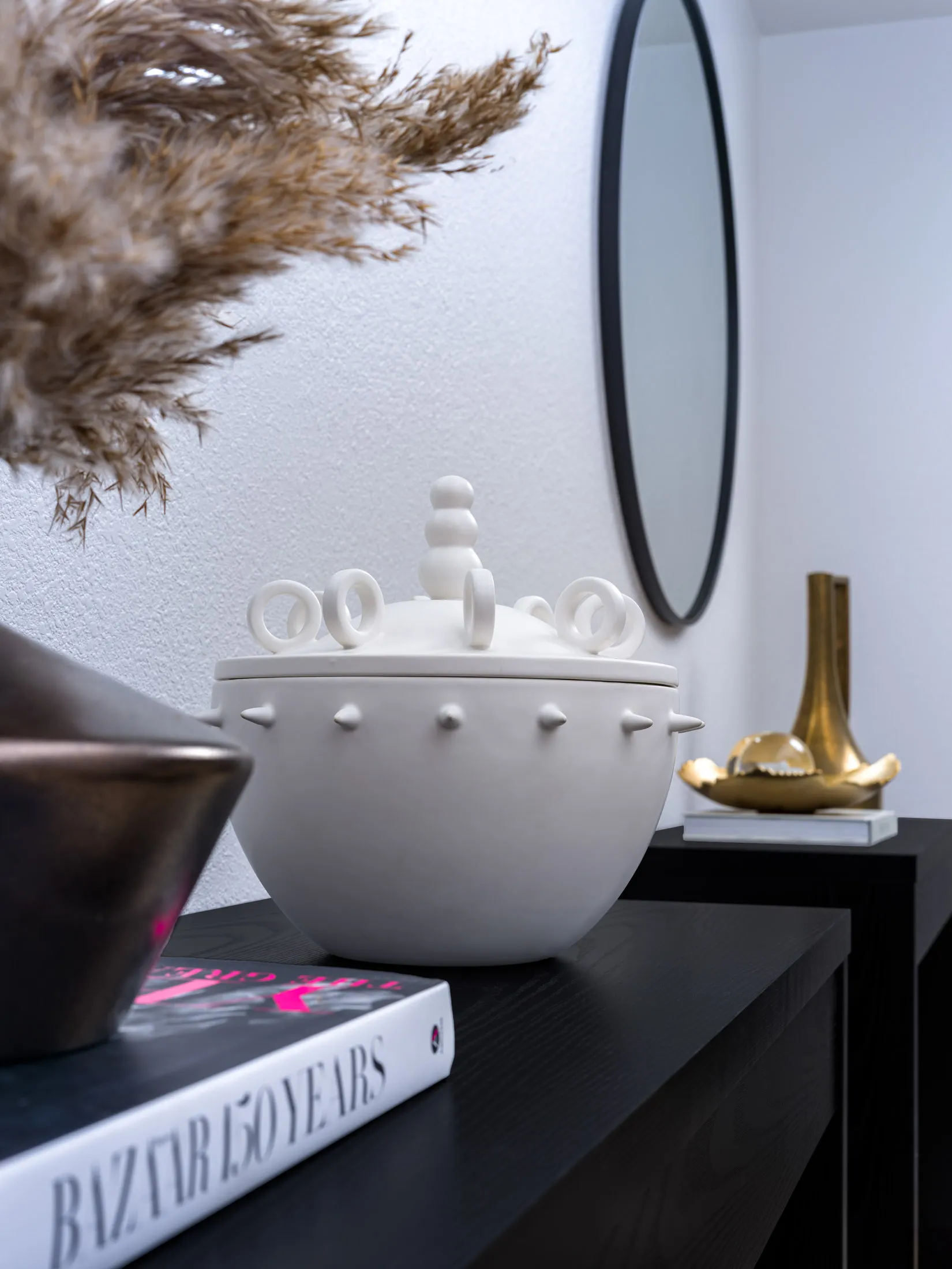 A white ceramic vessel with looped handles and studded details on a black console, surrounded by decorative accents.